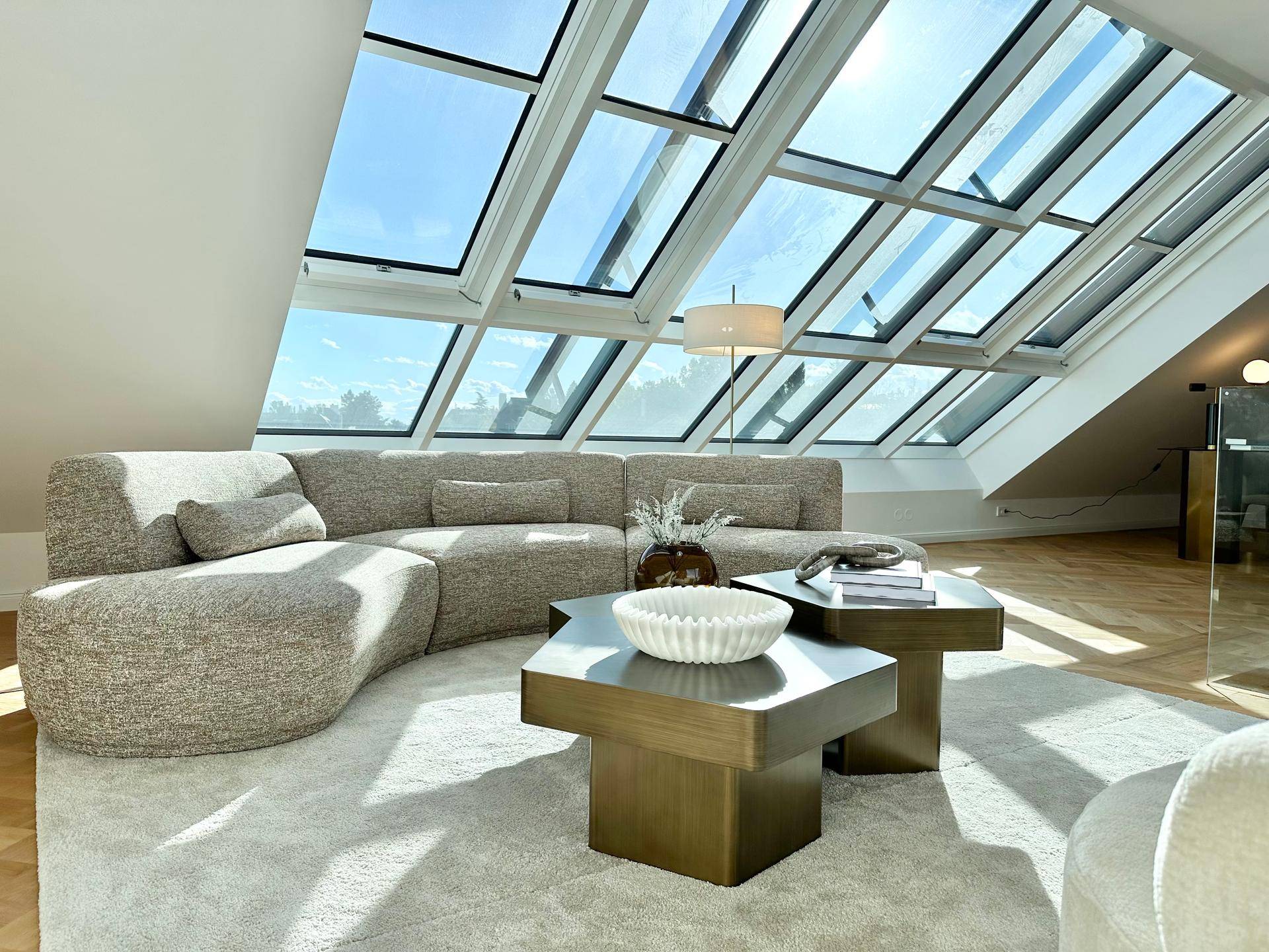 Lichtdurchflutetes Wohnzimmer im Dachgeschoss mit großer Fensterfront und modernem Sofa.