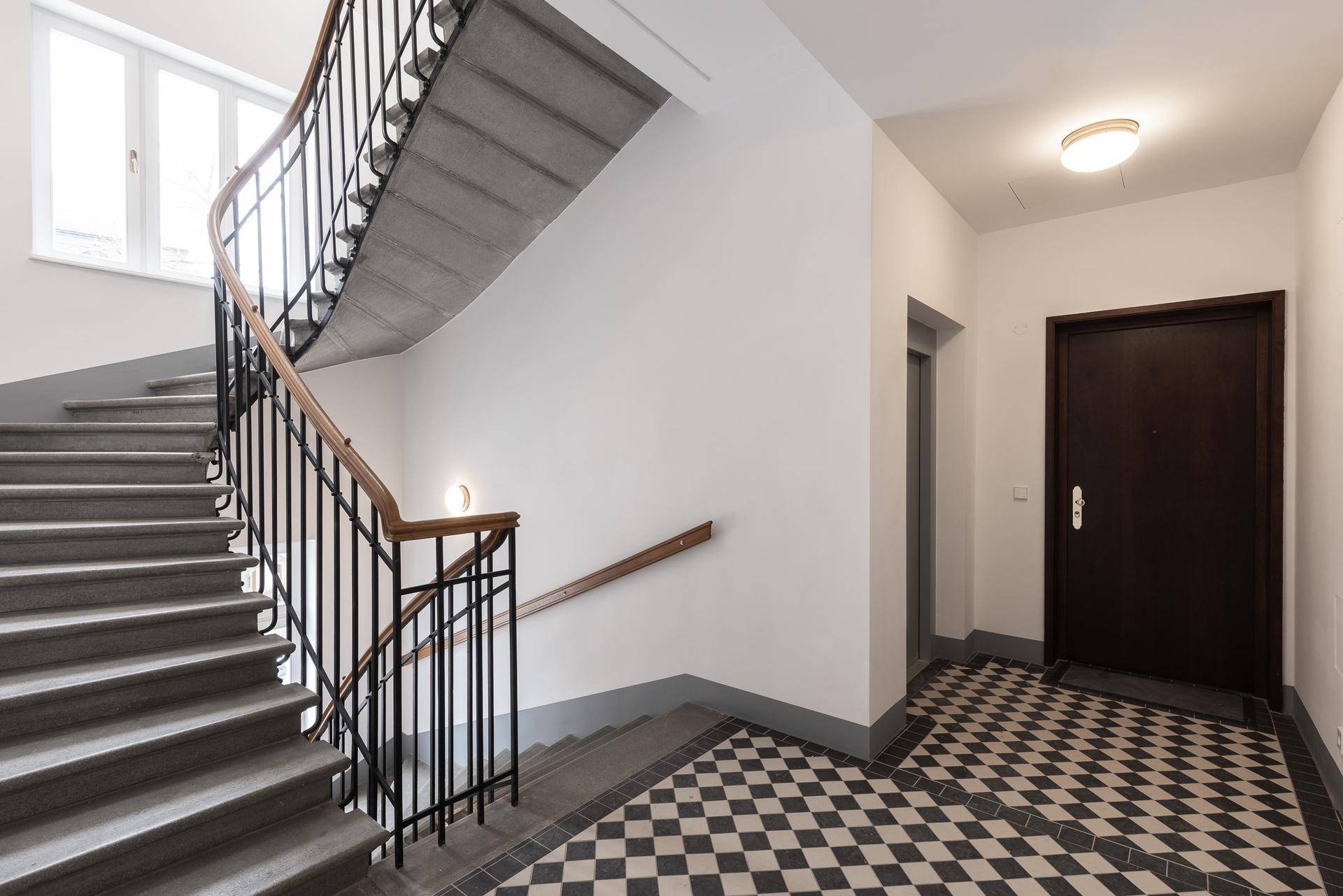 Historisches Treppenhaus mit geschwungener Steintreppe, schmiedeeisernem Geländer und Schachbrettboden.