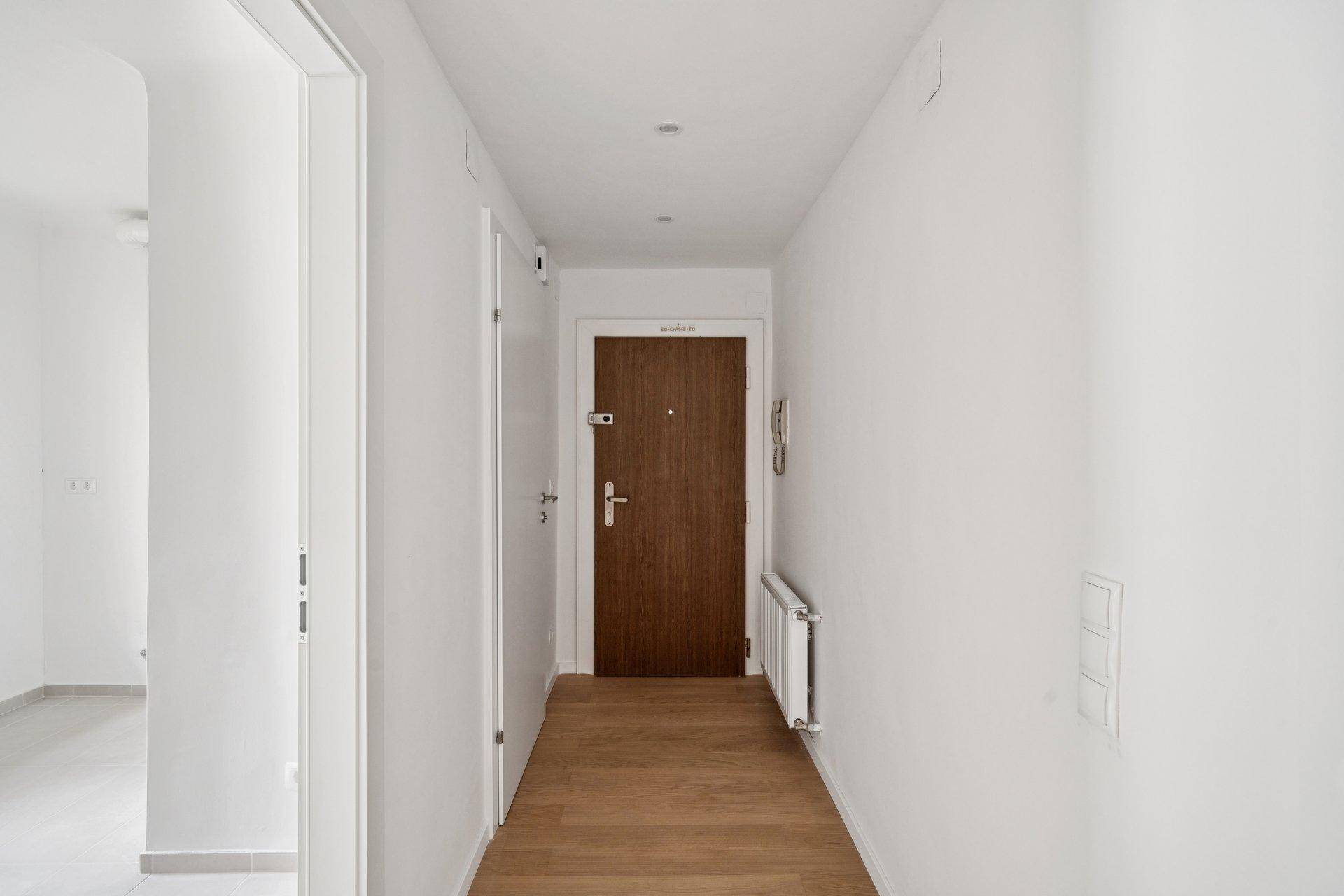 Langer Flur mit Holzboden, weiß gestrichenen Wänden und einer modernen Eingangstür.