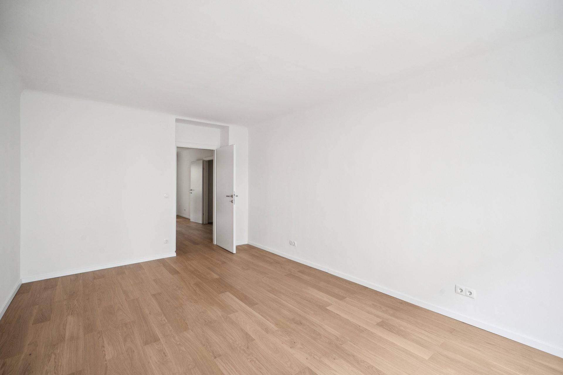Leeres Zimmer mit hellem Parkettboden und weiß gestrichenen Wänden, bereit zur individuellen Gestaltung.