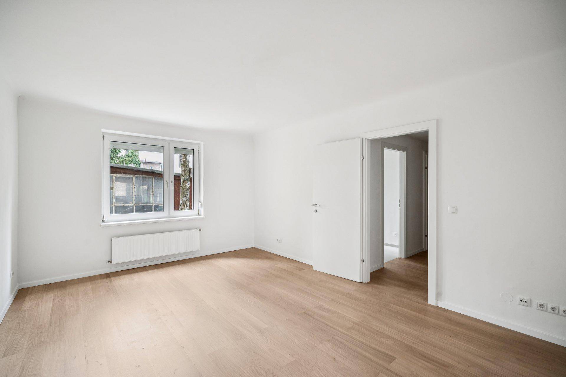 Geräumiges, leeres Zimmer mit hellem Parkettboden und großem Fenster, bereit zur Einrichtung.