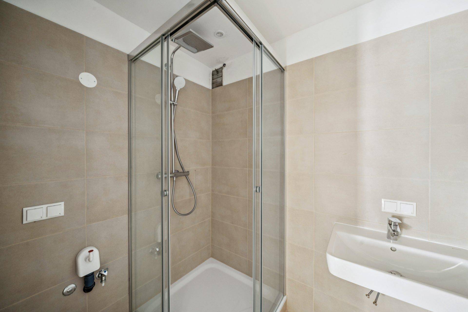 Modernes Badezimmer mit Duschkabine, Waschbecken und hellen Fliesen an Wänden und Boden.