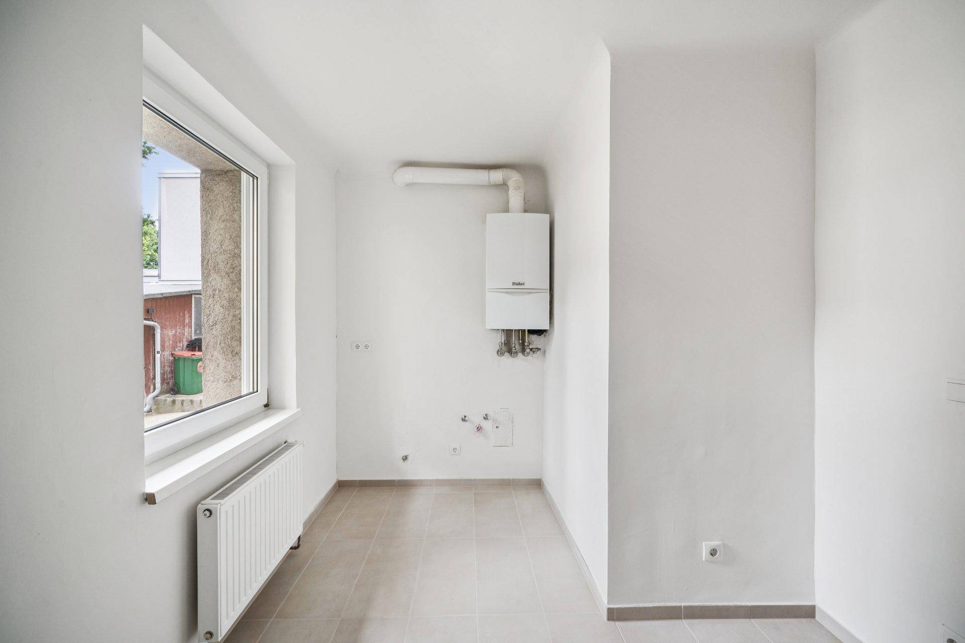 Hauswirtschaftsraum mit Fliesenboden, Fenster, Heizkörper und wandmontierter Heizungsanlage.