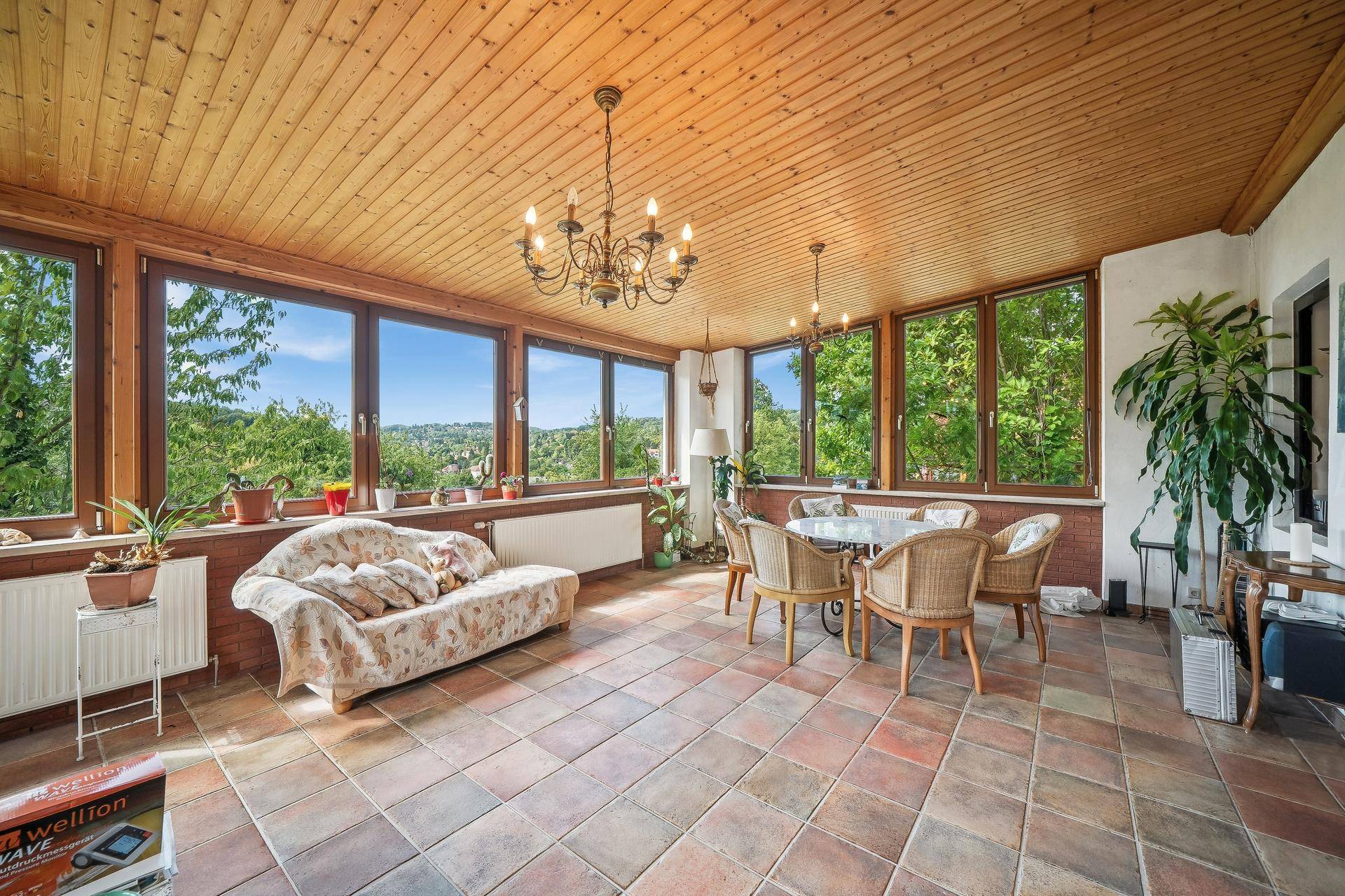 Heller Wintergarten mit Fliesenboden, Holzdecke und weitem Blick ins Grüne.