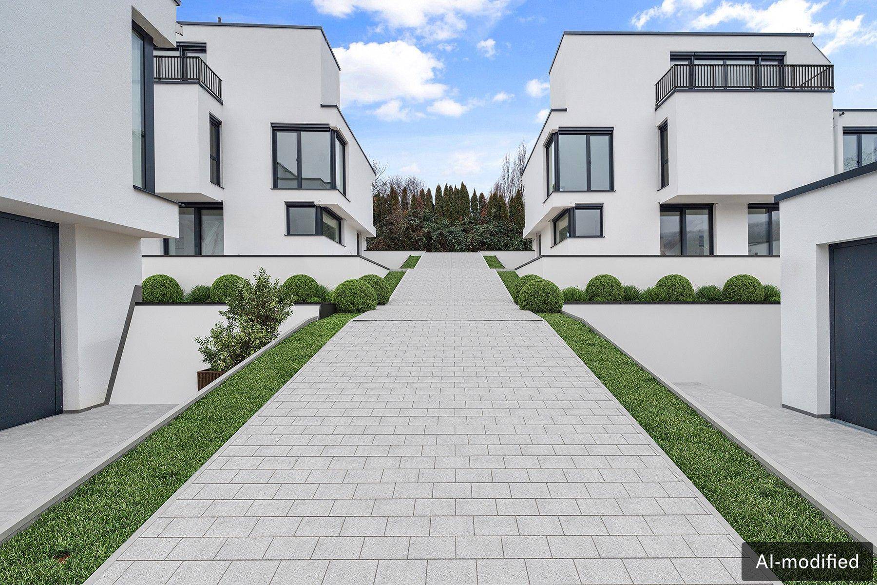 Moderne Wohnanlage mit weißer Fassade, großen Fenstern und gepflasterter Zufahrt.