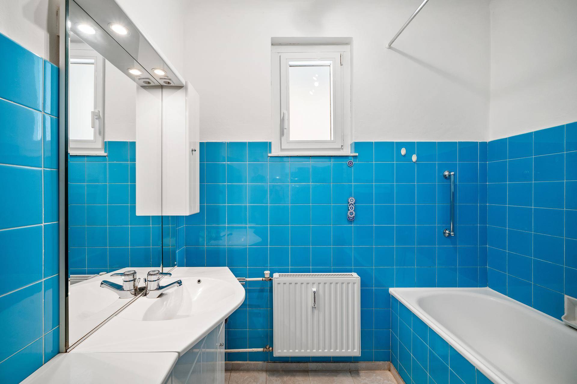 Badezimmer mit blauen Fliesen, Badewanne, Waschbecken und einem Fenster für Tageslicht.