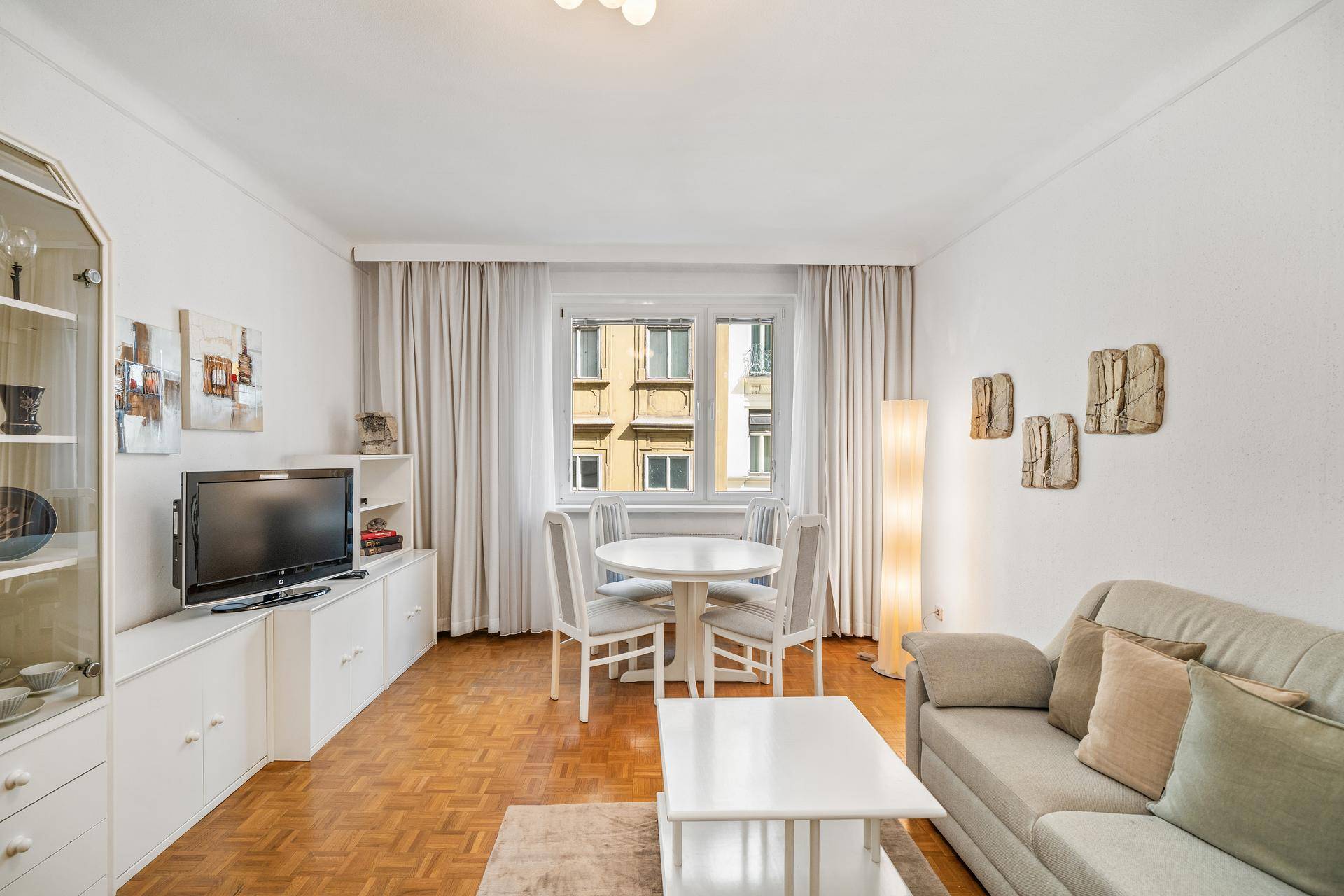 Gemütlicher Wohn- und Essbereich mit Parkettboden, hellem Sofa und Esstisch am Fenster.