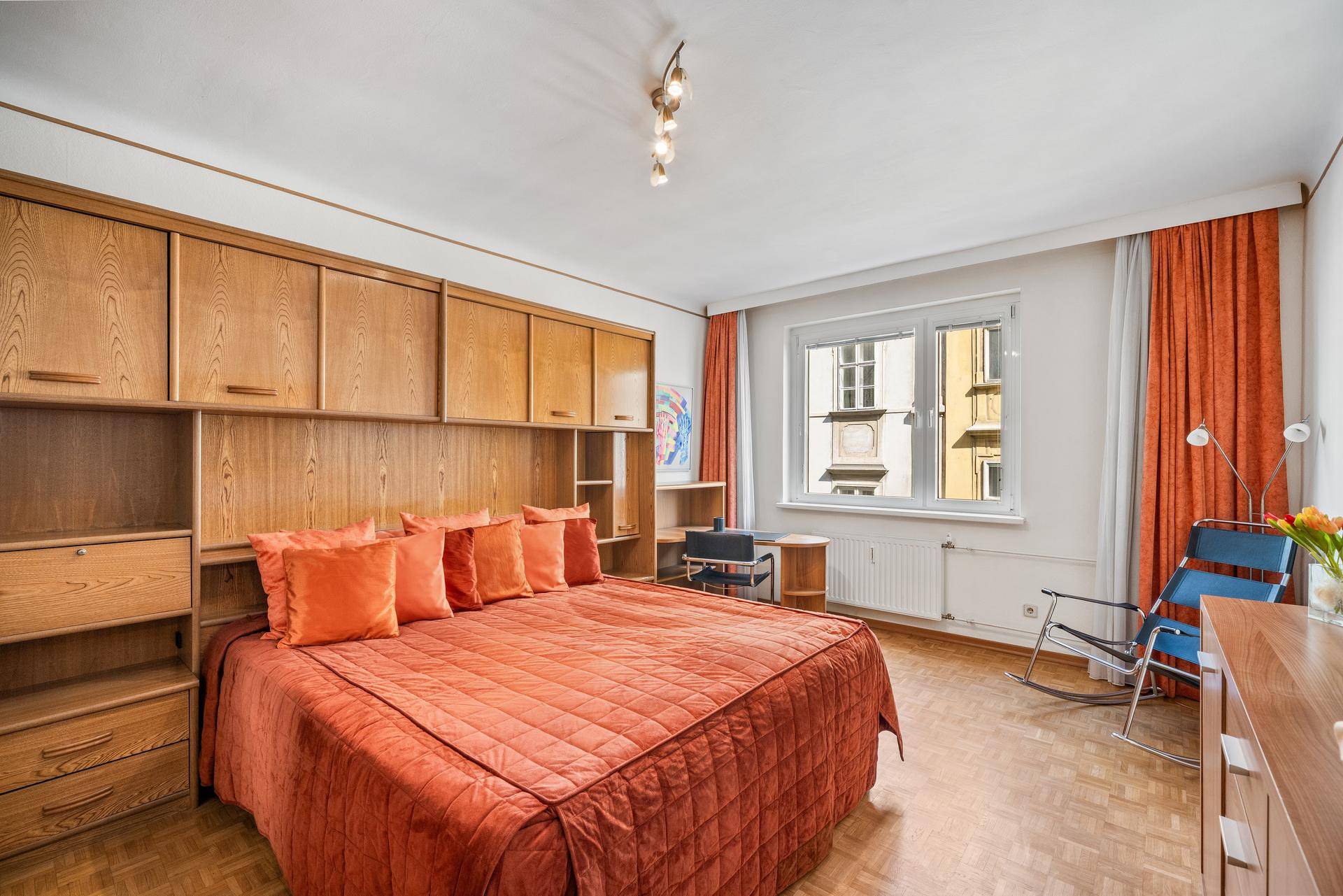 Schlafzimmer mit großem Bett, Holzschränken und Parkettboden, hell durch das Fenster.