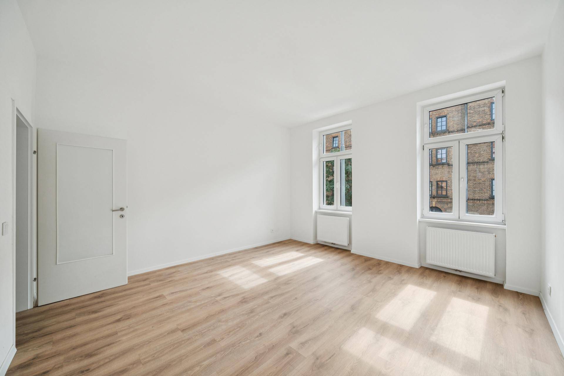 Geräumiges, helles Zimmer mit Laminatboden und weißer Tür, bereit zur individuellen Gestaltung.