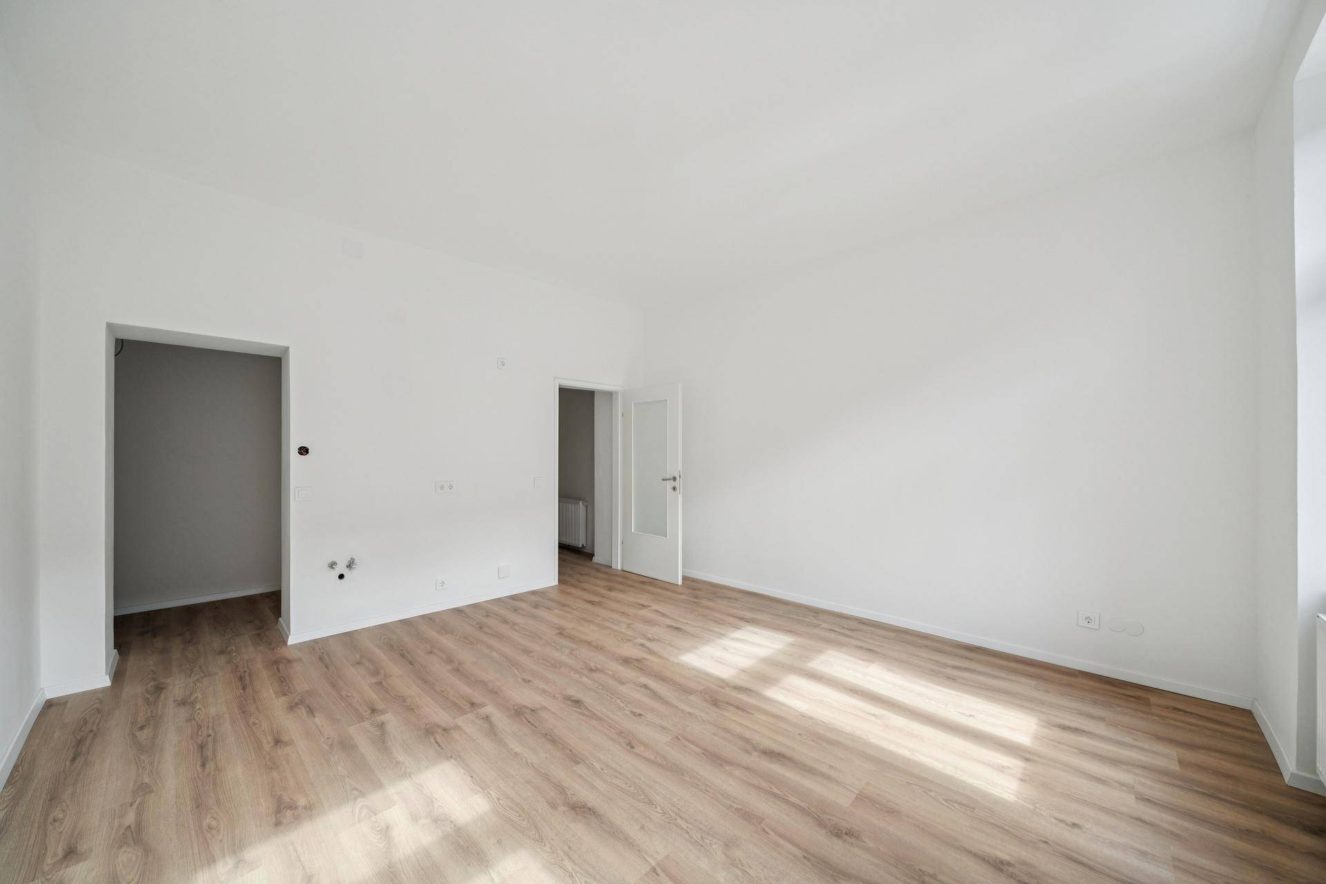 Leerer Raum mit Laminatboden und zwei Türöffnungen, die zu weiteren Zimmern führen.