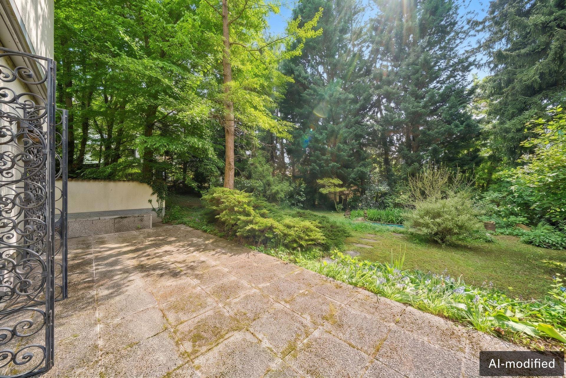 Gepflasterte Terrasse mit schmiedeeisernem Tor, die in einen weitläufigen Garten führt.