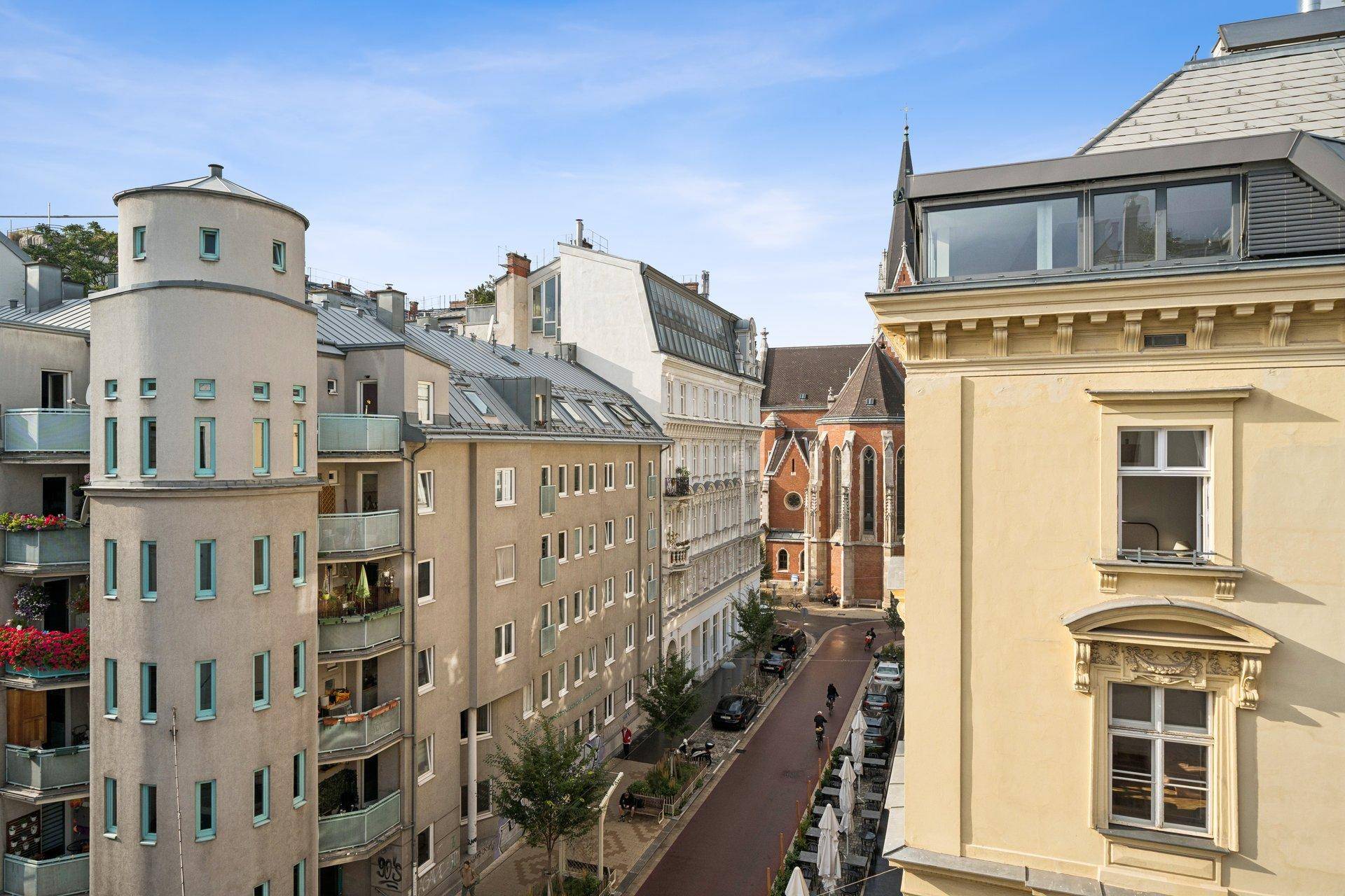 Blick auf eine belebte Stadtstraße mit historischen Gebäuden und einem Kirchturm im Hintergrund.