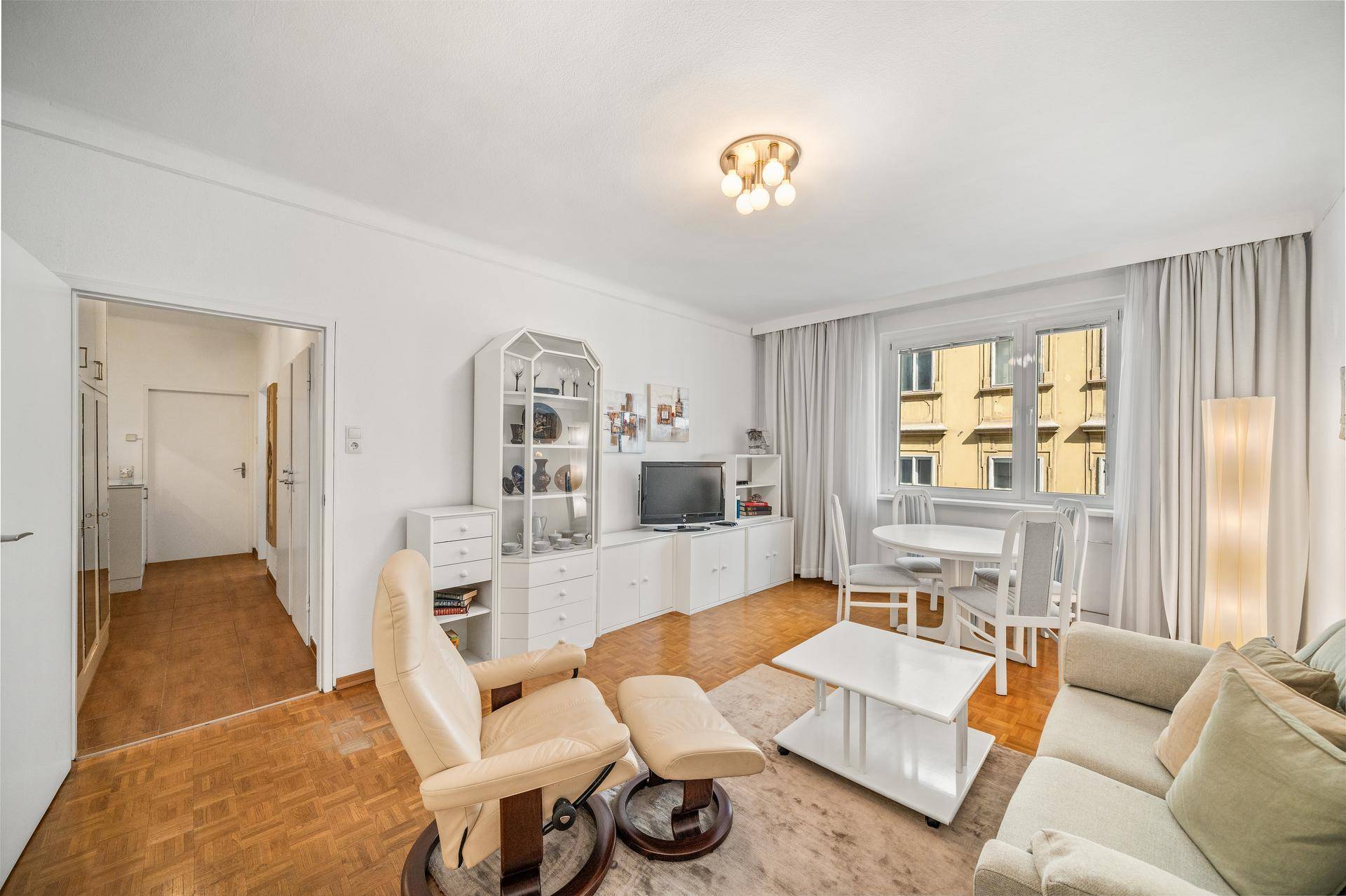 Helles Wohn- und Esszimmer mit Parkettboden, weißer Einrichtung und Blick auf die Stadt.