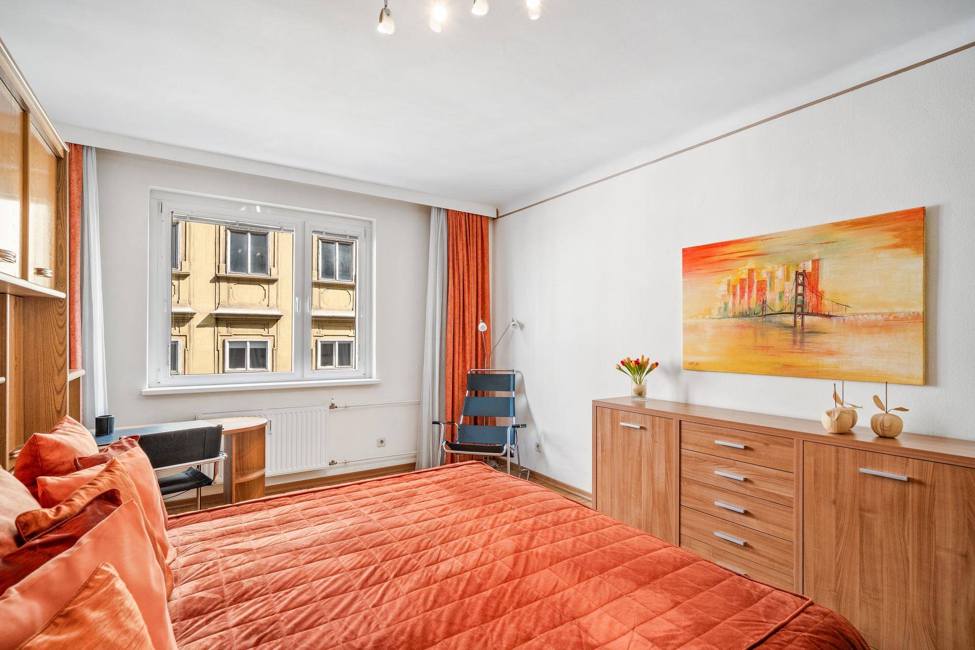 Geräumiges Schlafzimmer mit Holzschränken, Parkettboden und einem farbenfrohen Wandbild.