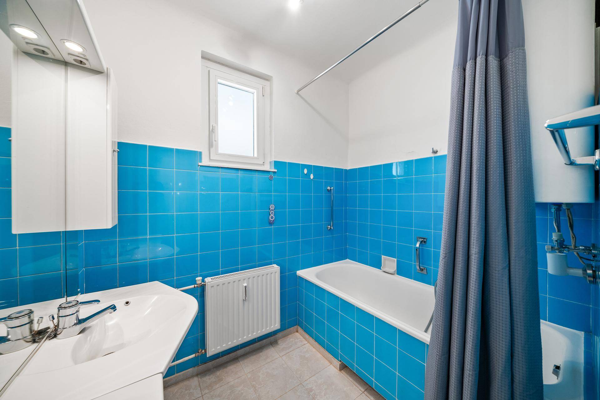 Badezimmer mit blauen Wandfliesen, Badewanne mit Duschvorhang und Waschbecken.