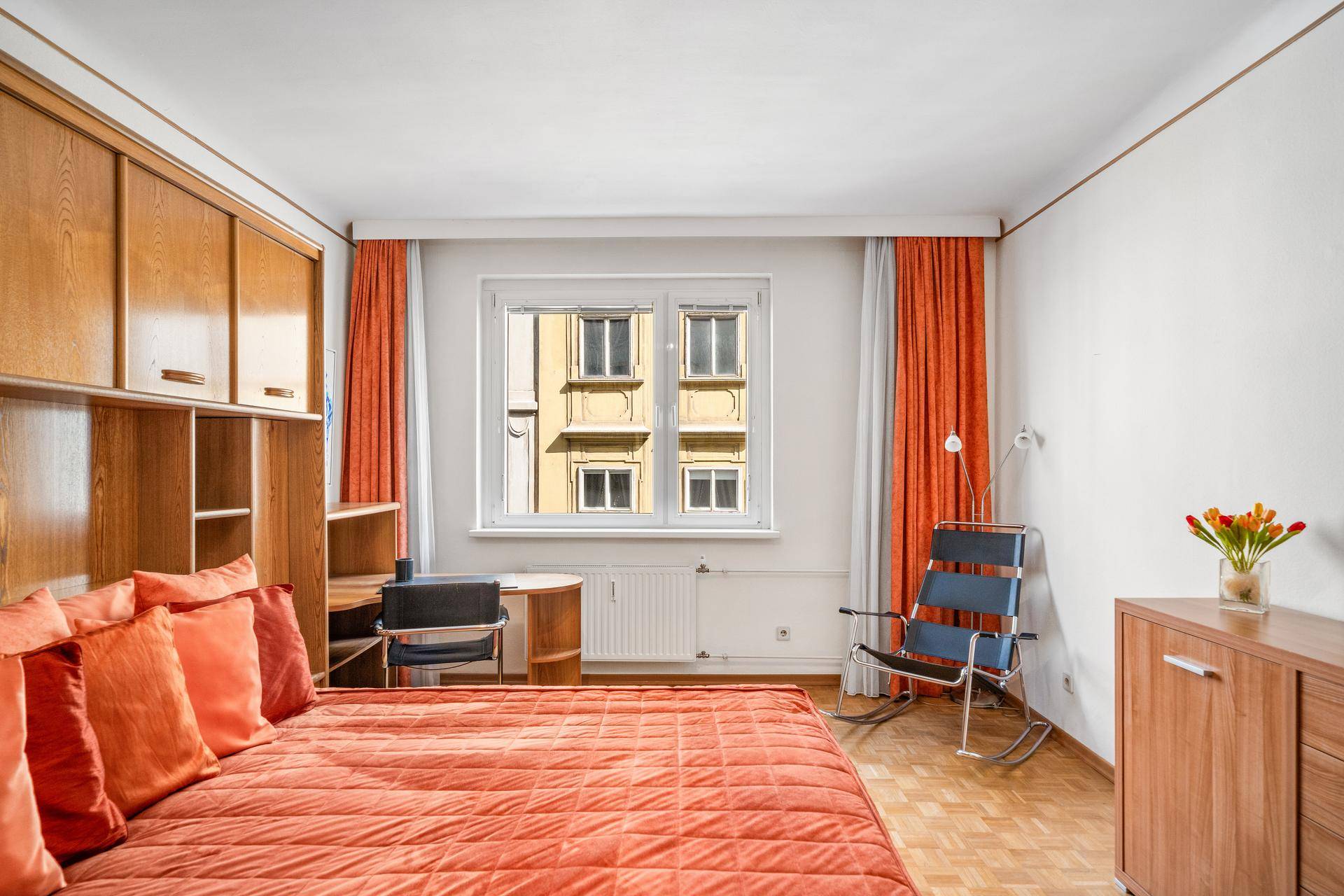 Helles Schlafzimmer mit Holzmöbeln, Parkettboden und einem Fenster mit Blick nach draußen.