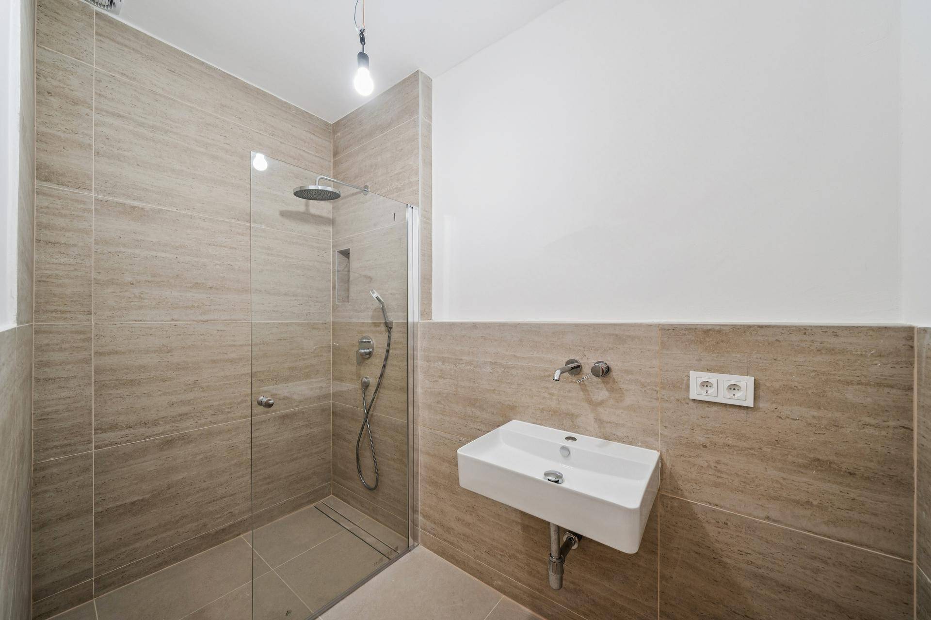 Modernes Badezimmer mit begehbarer Dusche, Wandwaschbecken und beigefarbenen Fliesen.