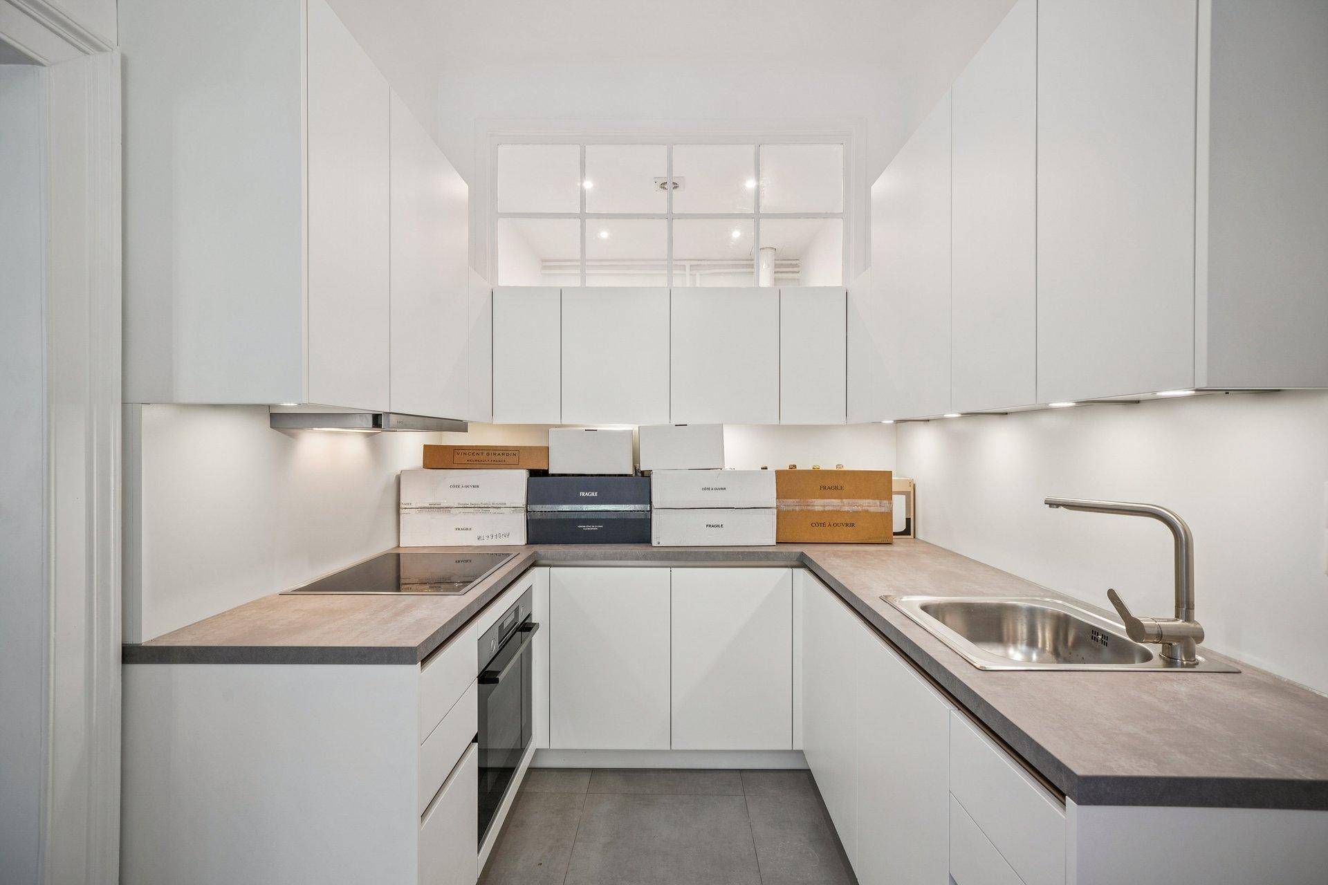 Moderne U-förmige Küche mit weißen Schränken, Induktionskochfeld und integriertem Backofen.