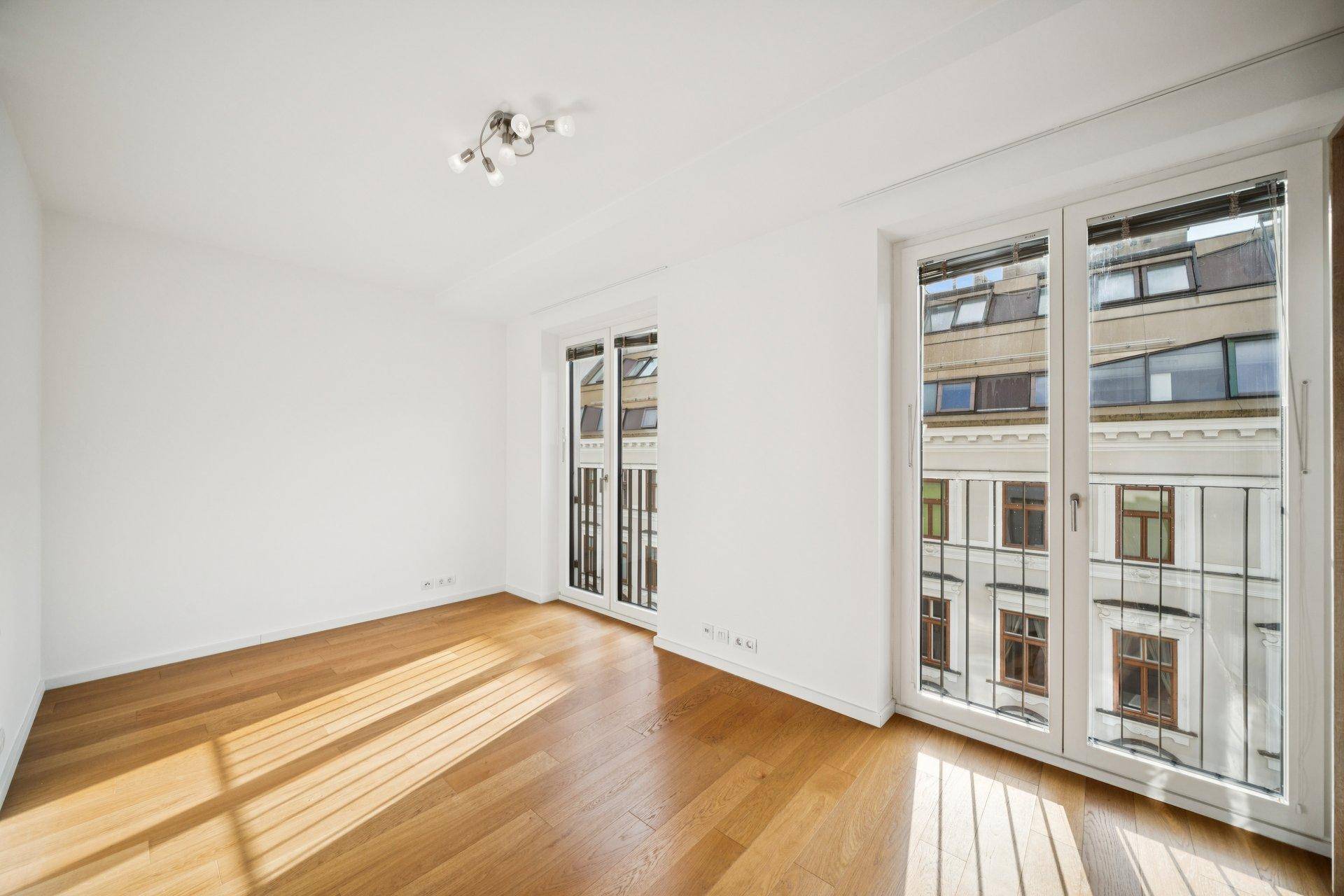 Helles, unmöbliertes Schlafzimmer mit Holzboden und großen Fenstern mit Stadtblick.