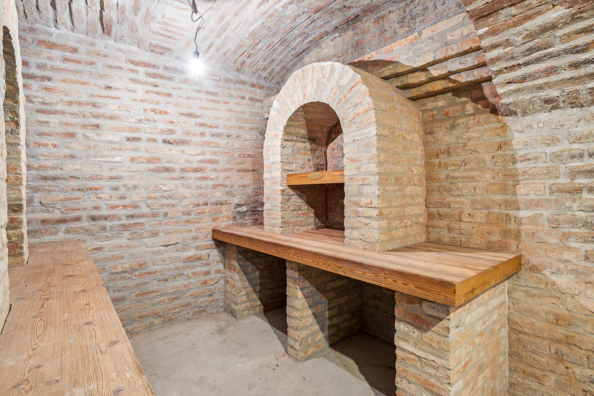 Rustikaler Gewölbekeller mit Ziegelwänden und Holzregalen, ideal zur Weinlagerung.