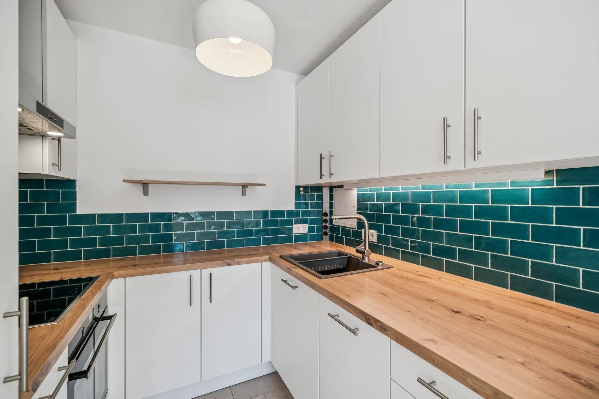 Moderne Küche mit weißen Schränken, Holz-Arbeitsplatten und türkisfarbenen Fliesen als Spritzschutz.