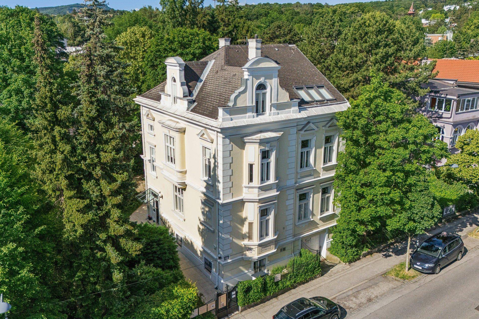 Historische Villa mit Mansarddach und reich verzierten Fassadendetails, umgeben von viel Grün.