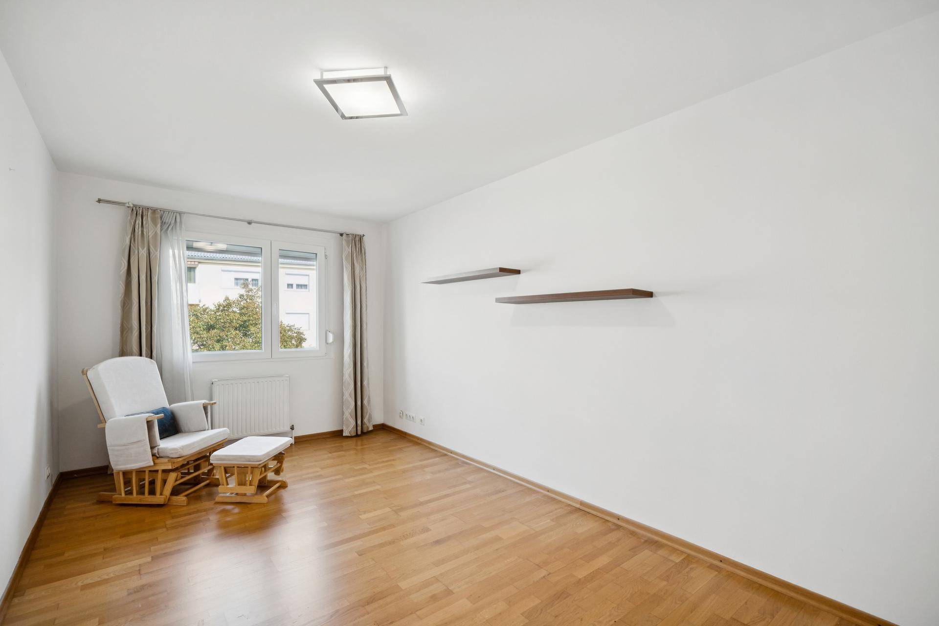 Helles Zimmer mit Parkettboden, großem Fenster und einem bequemen Schaukelstuhl.