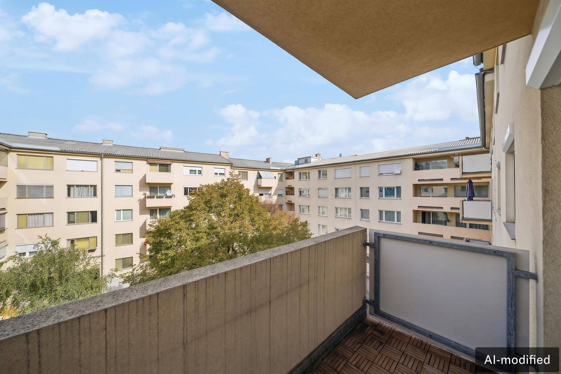 Balkon mit Holzboden und Blick auf die umliegenden Wohngebäude und grüne Bäume.