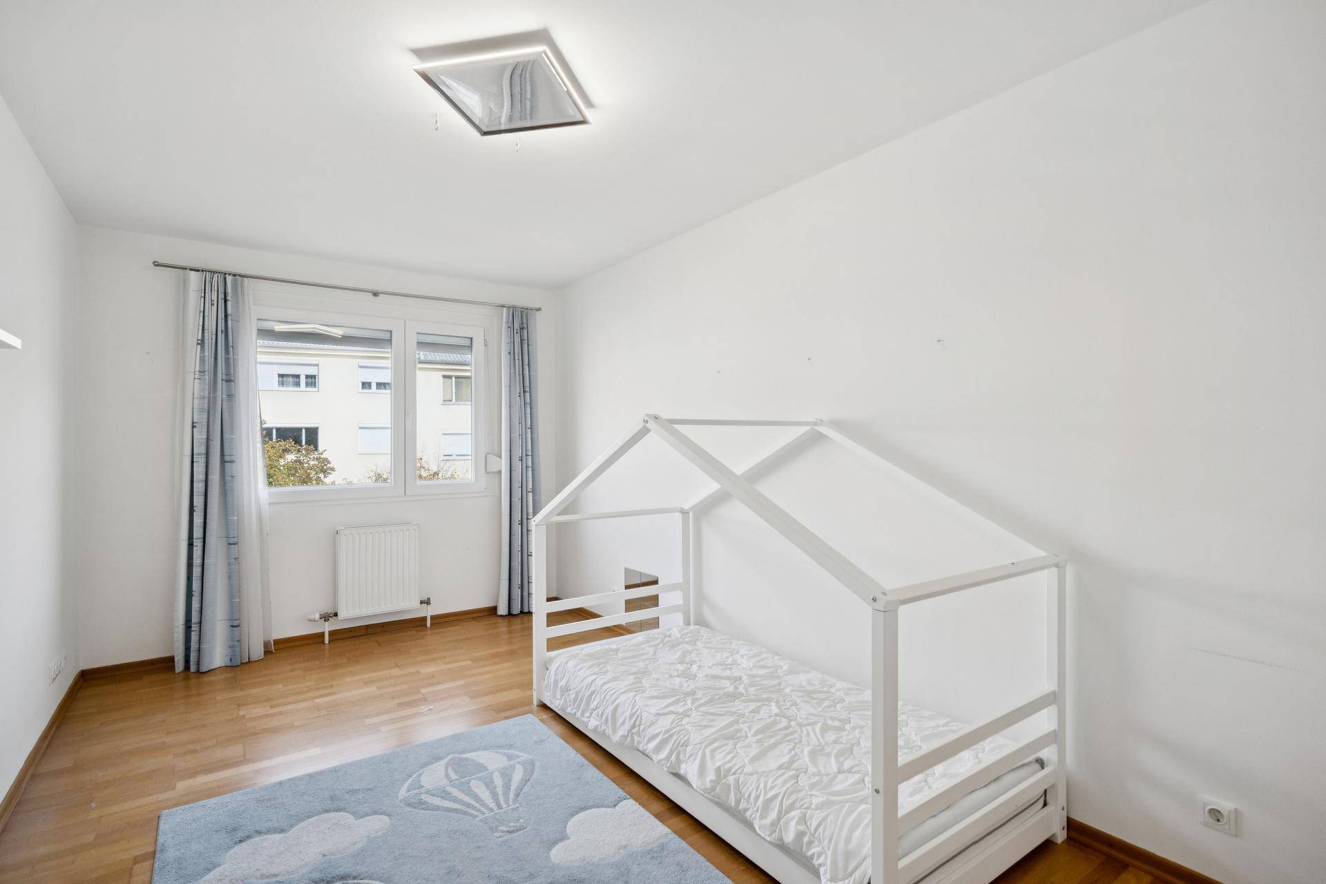 Kinderzimmer mit einem charmanten Hausbett, Parkettboden und einem farbenfrohen Teppich.