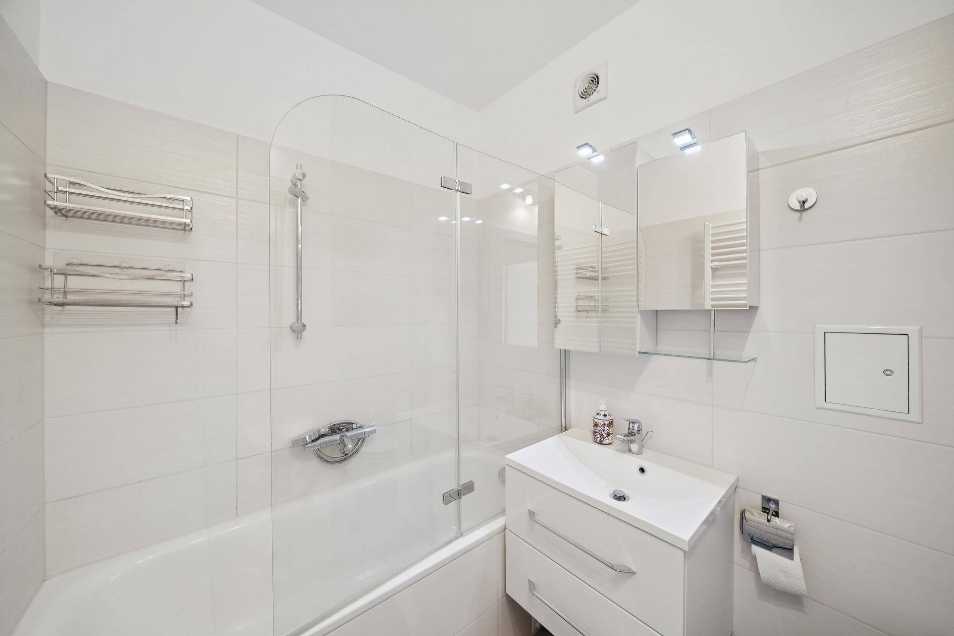 Modernes Badezimmer mit Badewanne, Duschwand, Einzelwaschbecken und Spiegelschrank.