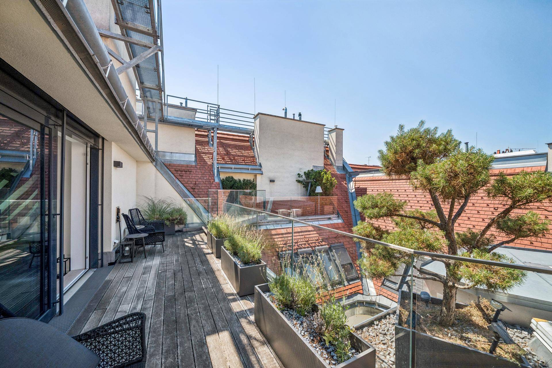 Weitläufige Dachterrasse mit Holzboden, Glasgeländer und grünen Pflanzen, ideal zum Entspannen.