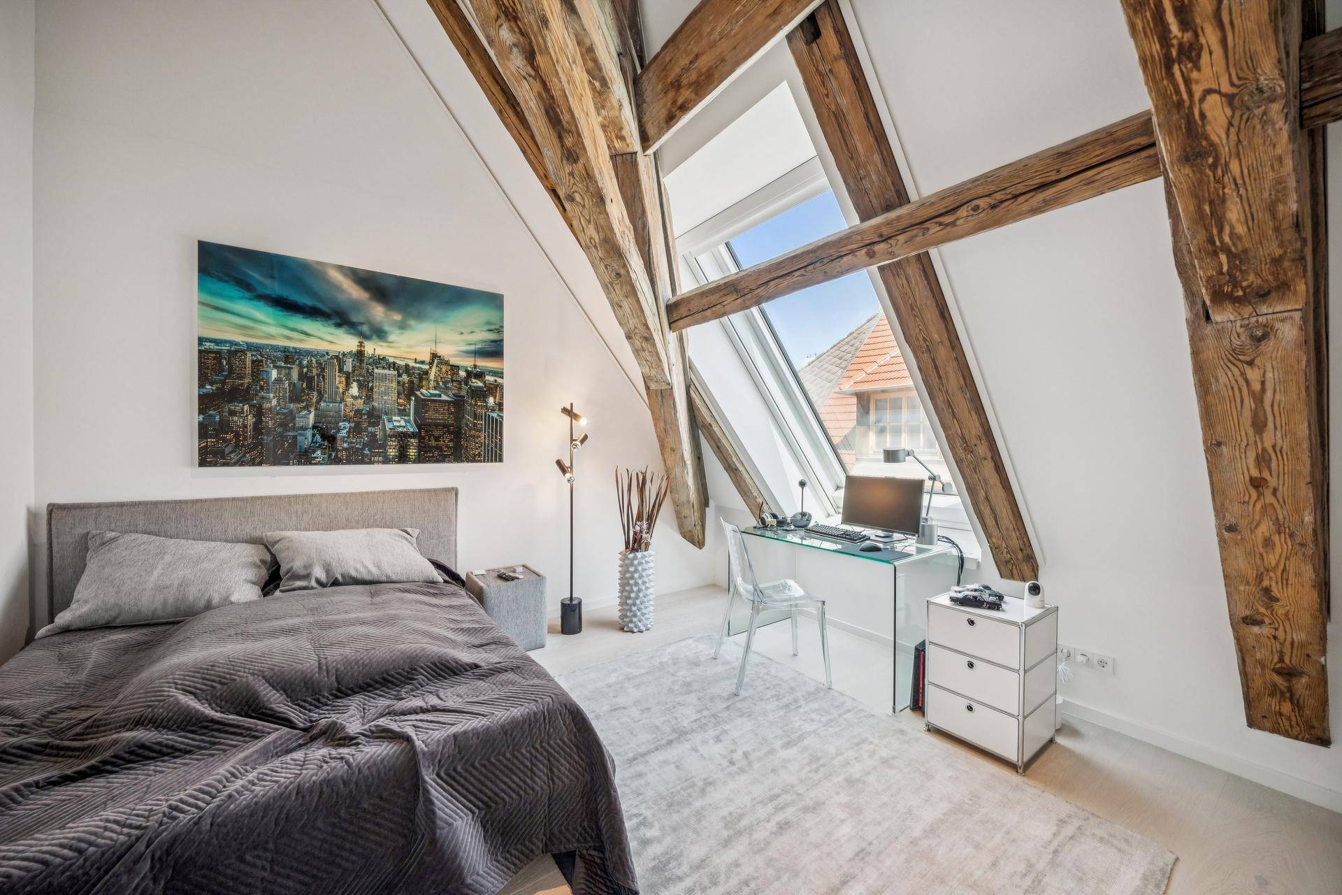 Gemütliches Schlafzimmer mit Arbeitsbereich, freiliegenden Holzbalken und viel Tageslicht durch das Dachfenster.