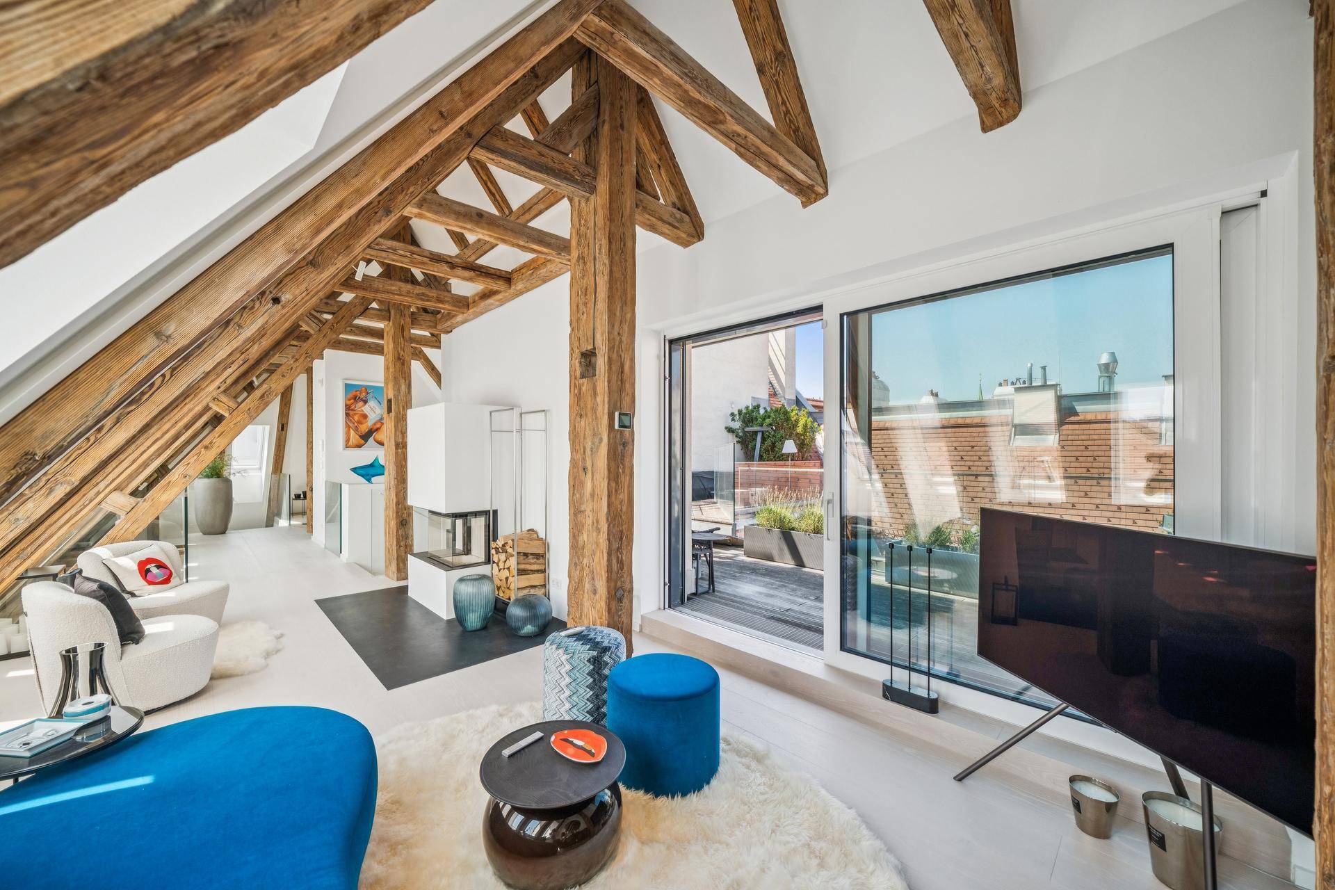 Helles Wohnzimmer mit modernem Kamin, Zugang zur Terrasse und beeindruckenden freiliegenden Holzbalken.