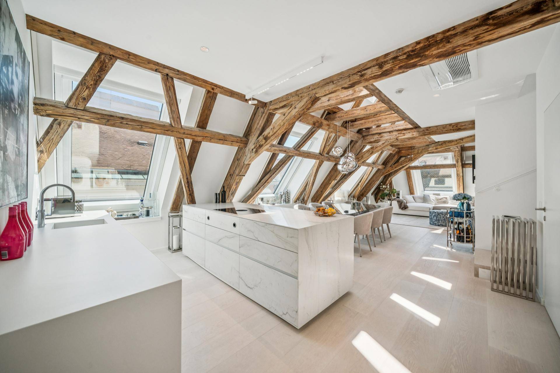 Moderne offene Wohnküche mit Marmorinsel, freiliegenden Holzbalken und viel Tageslicht durch Dachfenster.