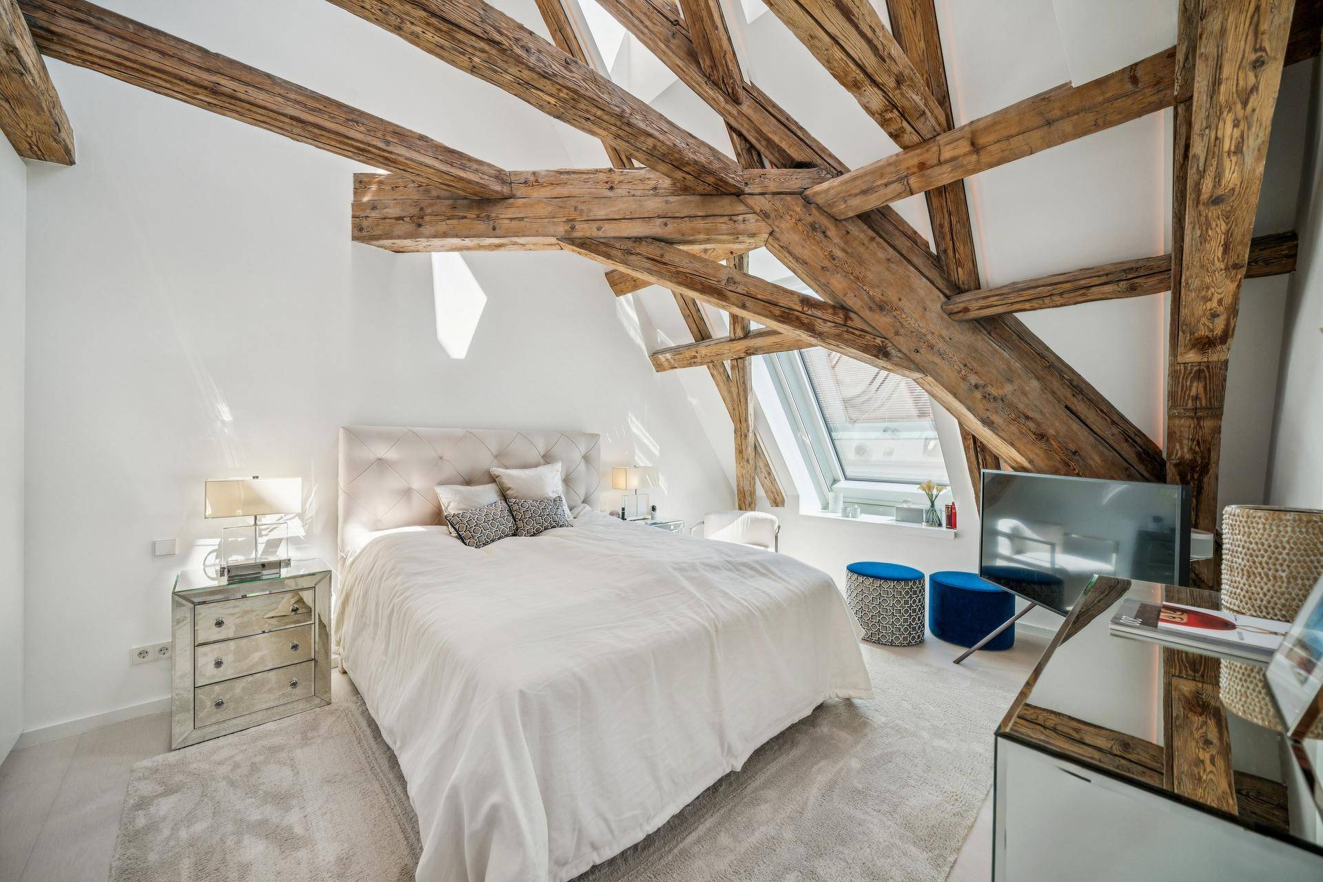 Helles Schlafzimmer im Dachgeschoss mit freiliegenden Holzbalken, gemütlichem Bett und Dachfenster.