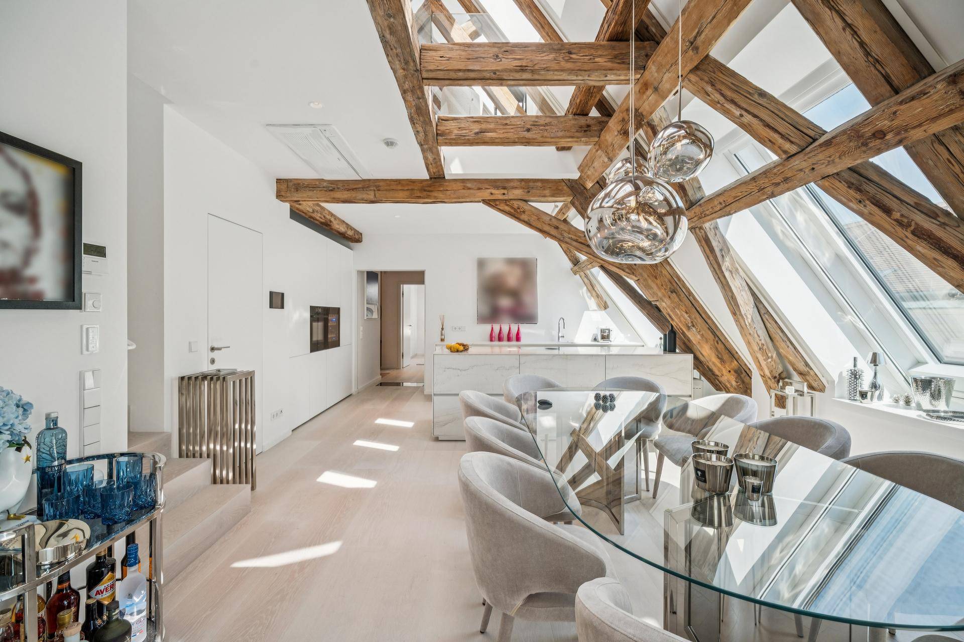 Eleganter Essbereich mit Glastisch und moderner Küche, umgeben von freiliegenden Holzbalken und Dachfenstern.