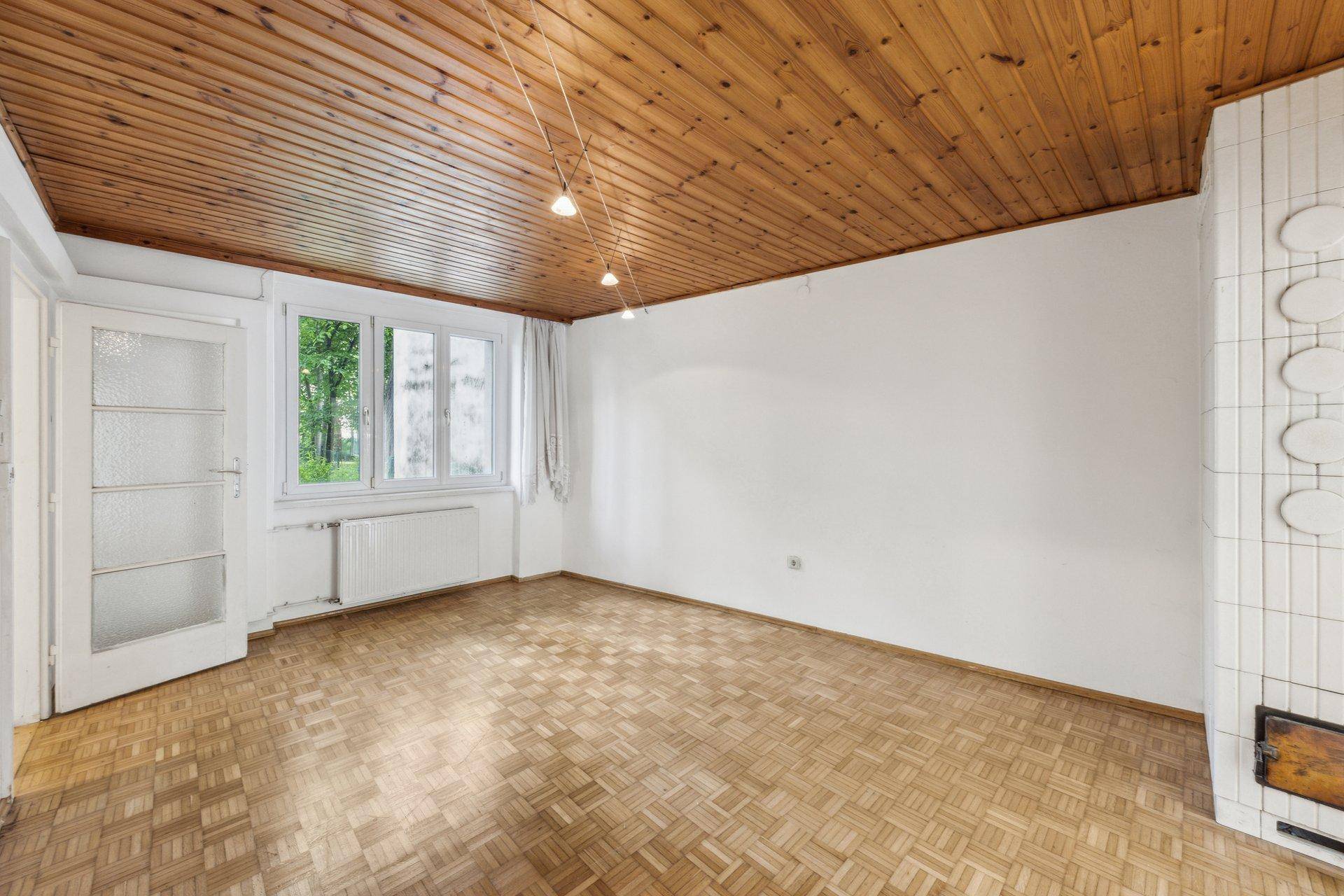 Gemütliches Zimmer mit Holzbalkendecke, Parkettboden und traditionellem Kachelofen.