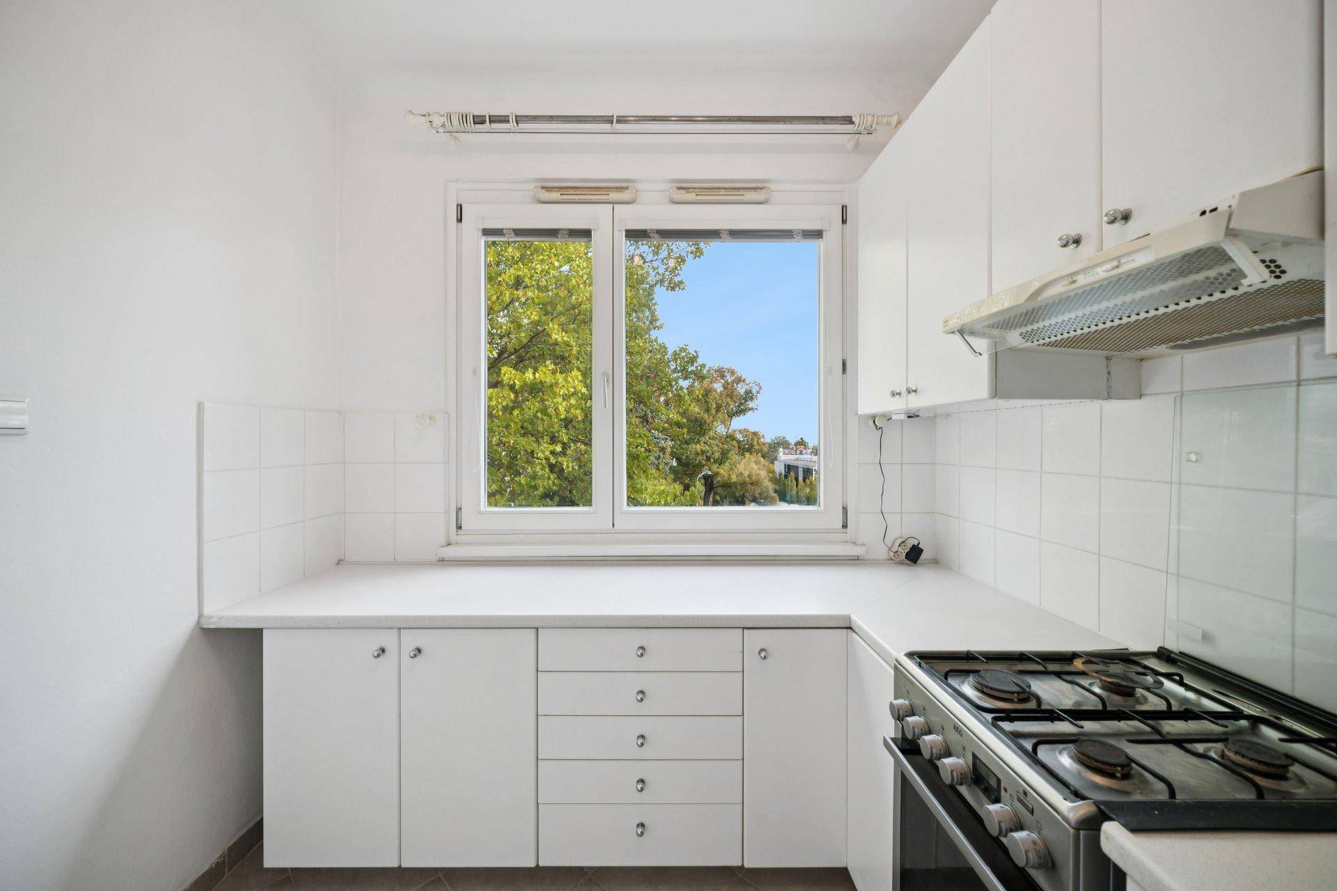 Funktionale Küche mit weißen Schränken, Gasherd und Fenster mit Blick ins Grüne.