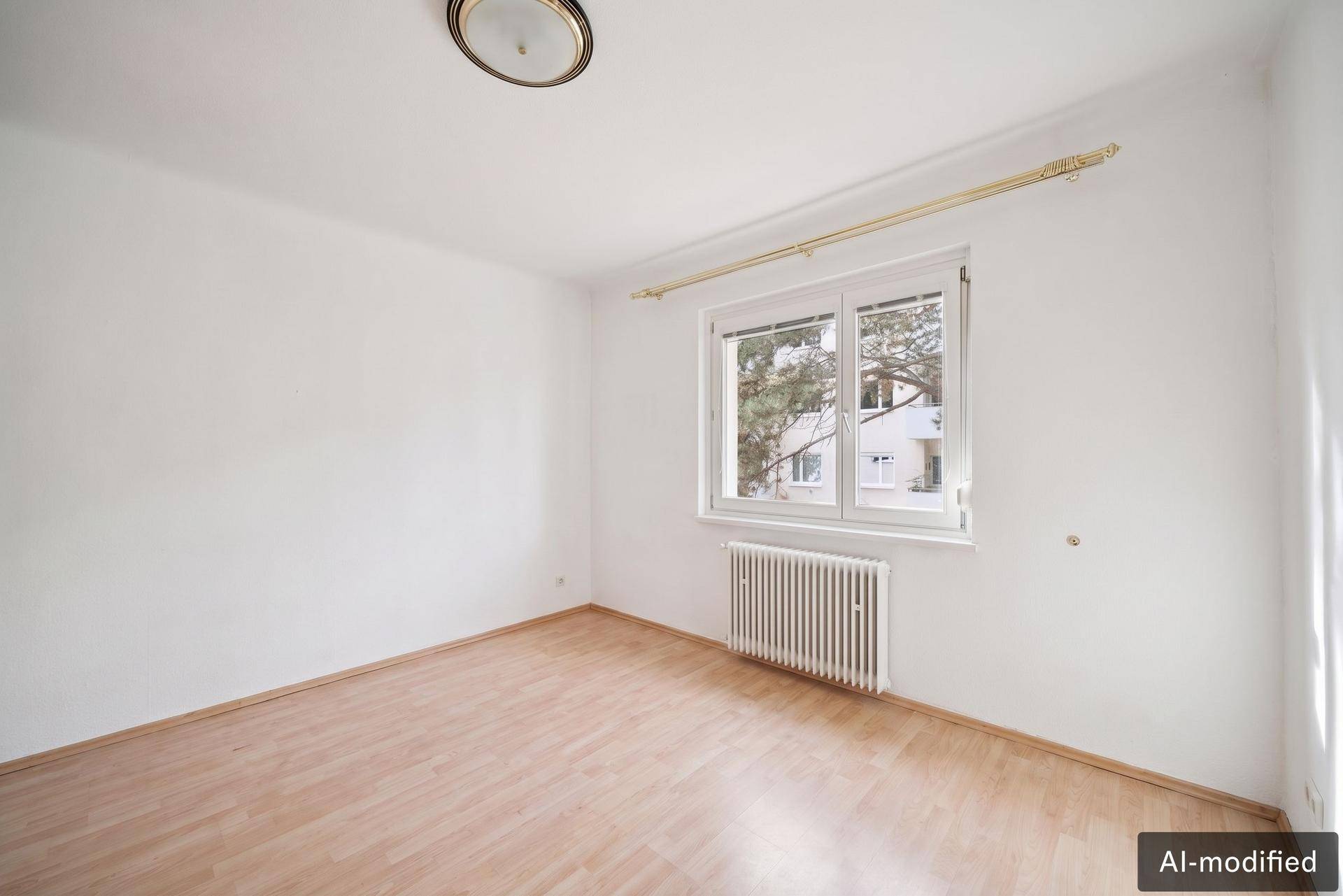Unmöbliertes Zimmer mit Parkettboden und Fenster, das einen Blick ins Grüne bietet.