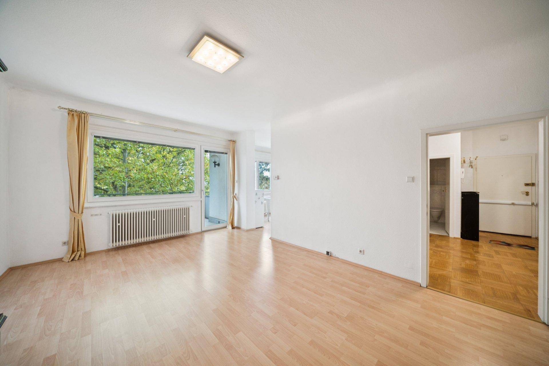 Geräumiges Wohnzimmer mit Parkettboden und Zugang zum Balkon, unmöbliert.