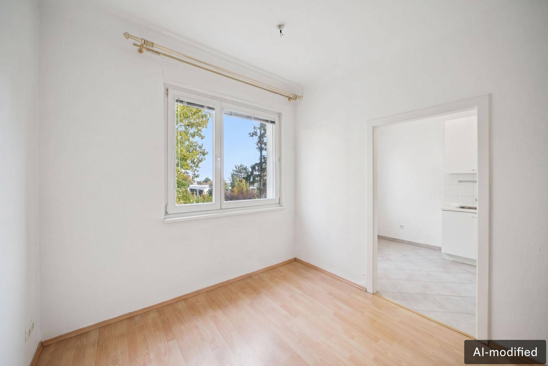 Leeres Zimmer mit Parkettboden und Fenster, das viel Tageslicht hereinlässt.