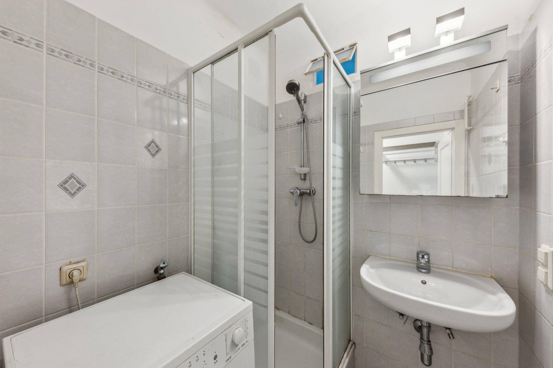 Funktionales Badezimmer mit Dusche, Waschbecken und Waschmaschine, hell gefliest.