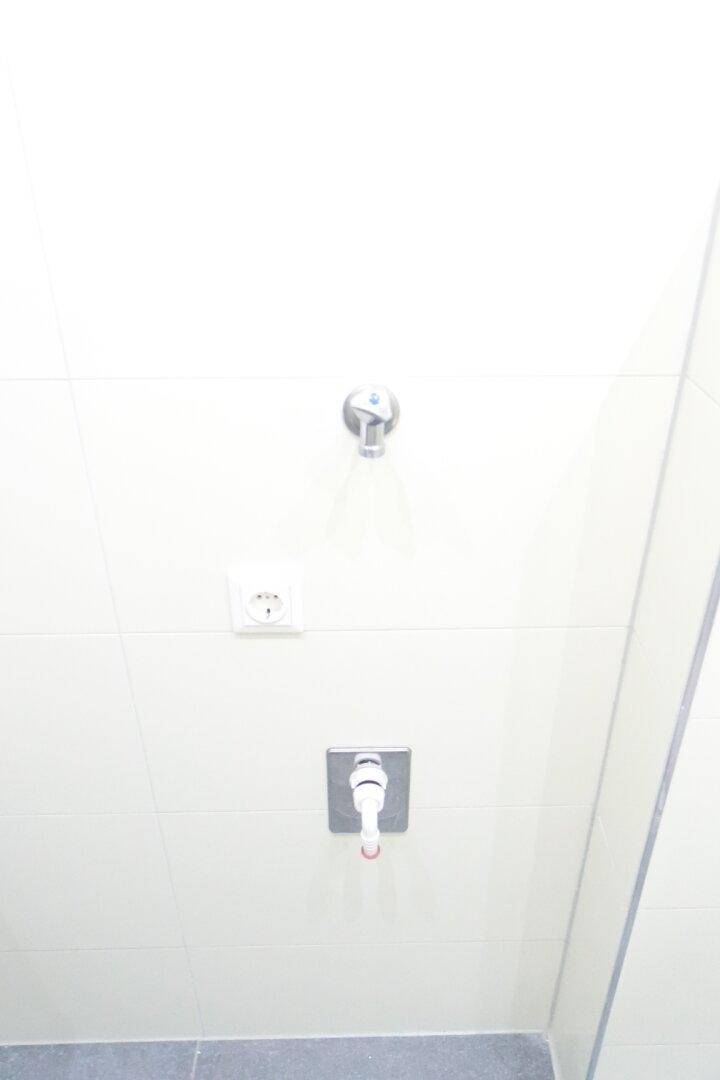Detailaufnahme einer Badezimmerwand mit Duscharmatur und Steckdose.