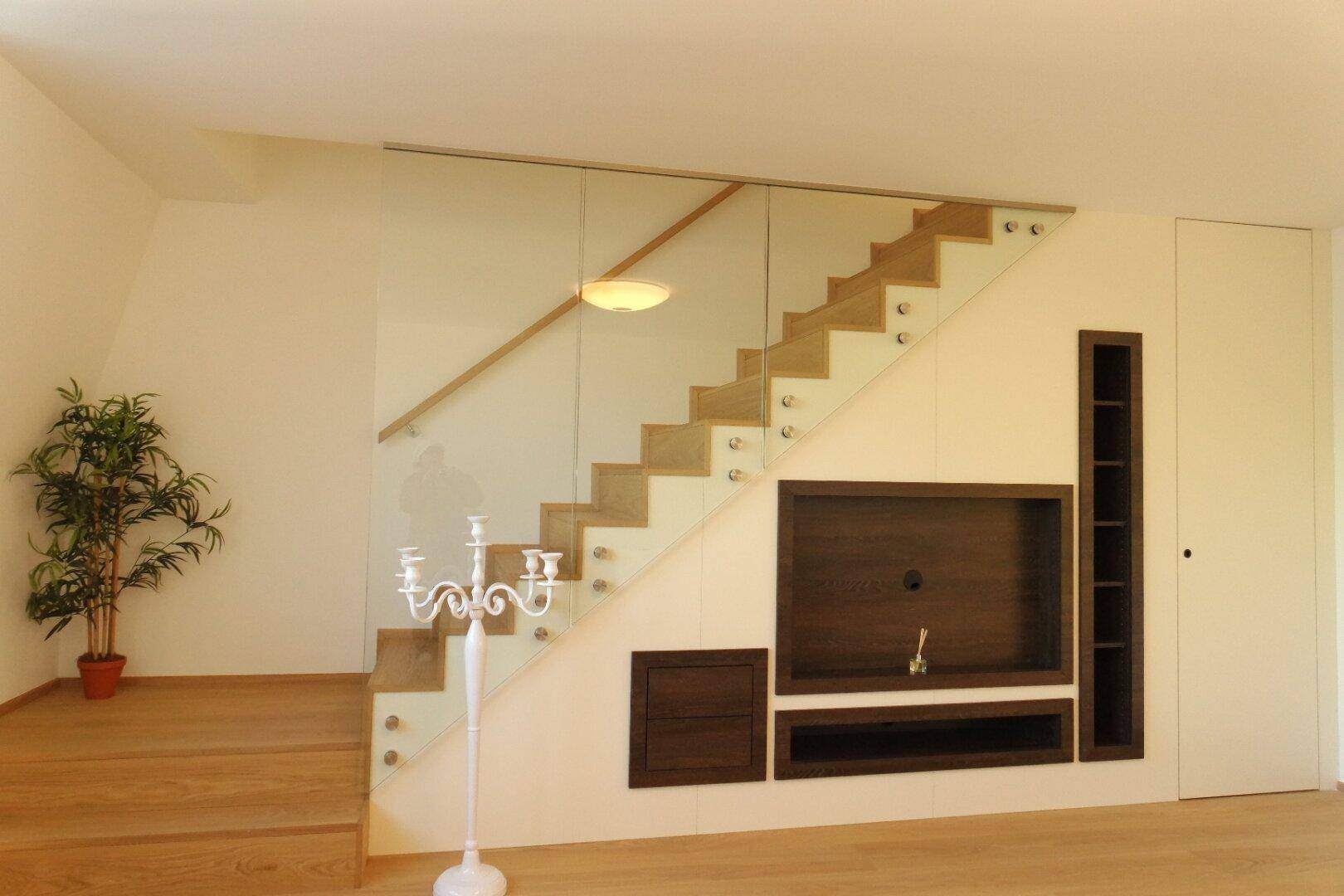 Moderner Treppenaufgang mit Glasgeländer, Holzstufen und integriertem Medienelement.
