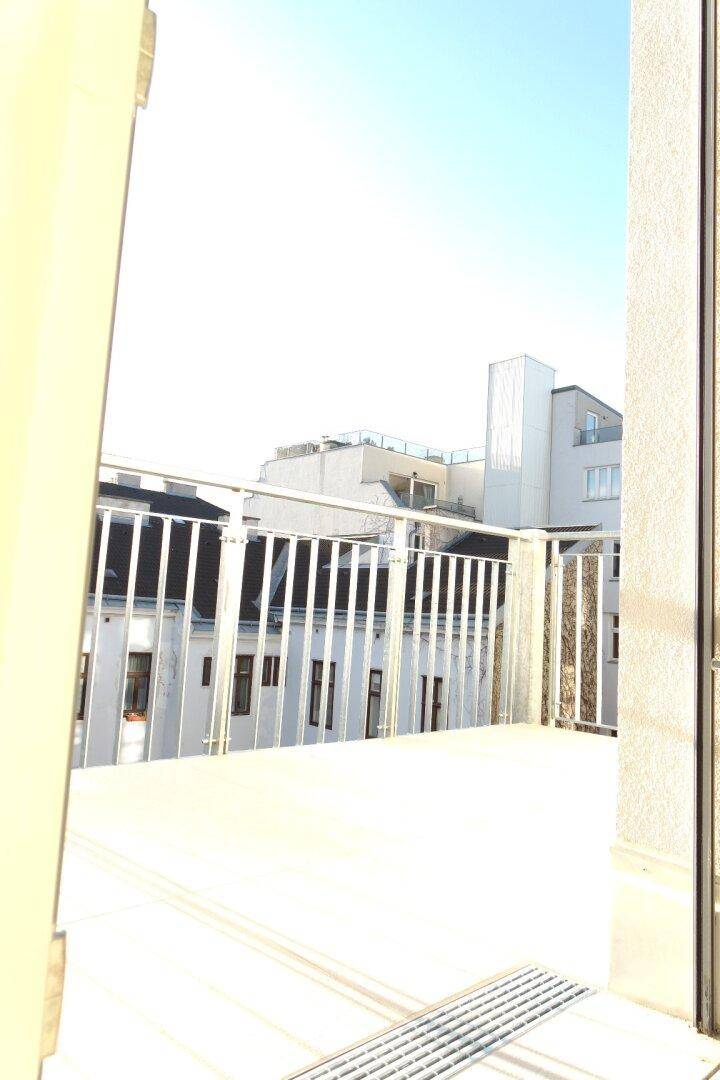 Balkon mit Metallgeländer und Blick auf umliegende Gebäude unter blauem Himmel.