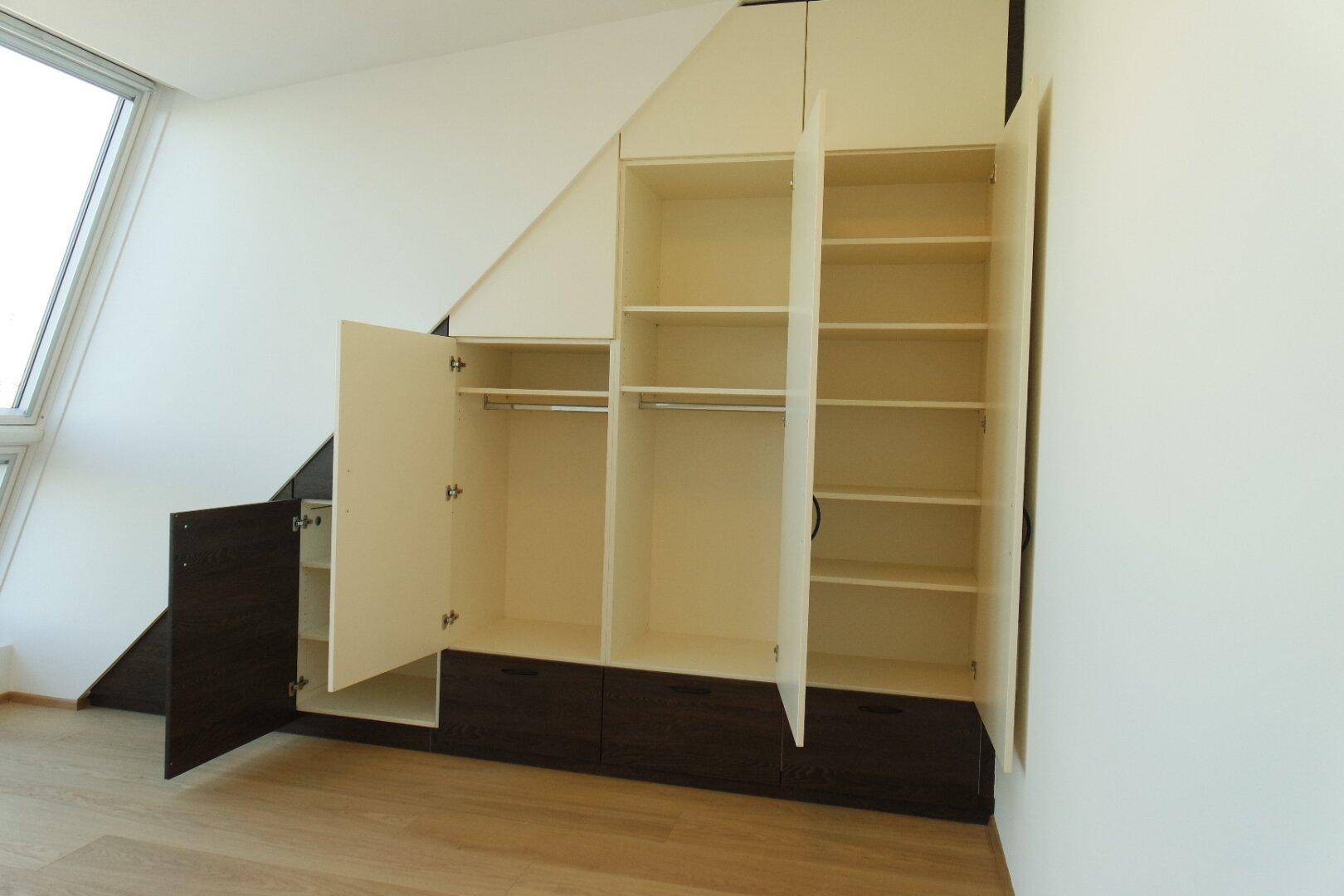 Maßgefertigte Einbauschränke mit offenen Türen und Regalen unter einer Dachschräge.