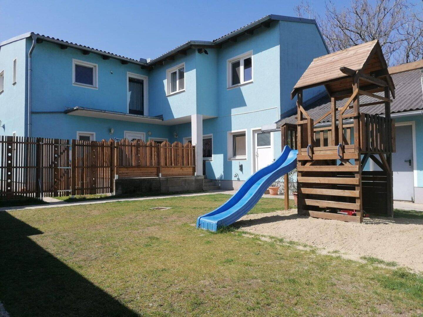Außenansicht des Hauses mit blauem Anstrich und einem Spielplatz im Gartenbereich.
