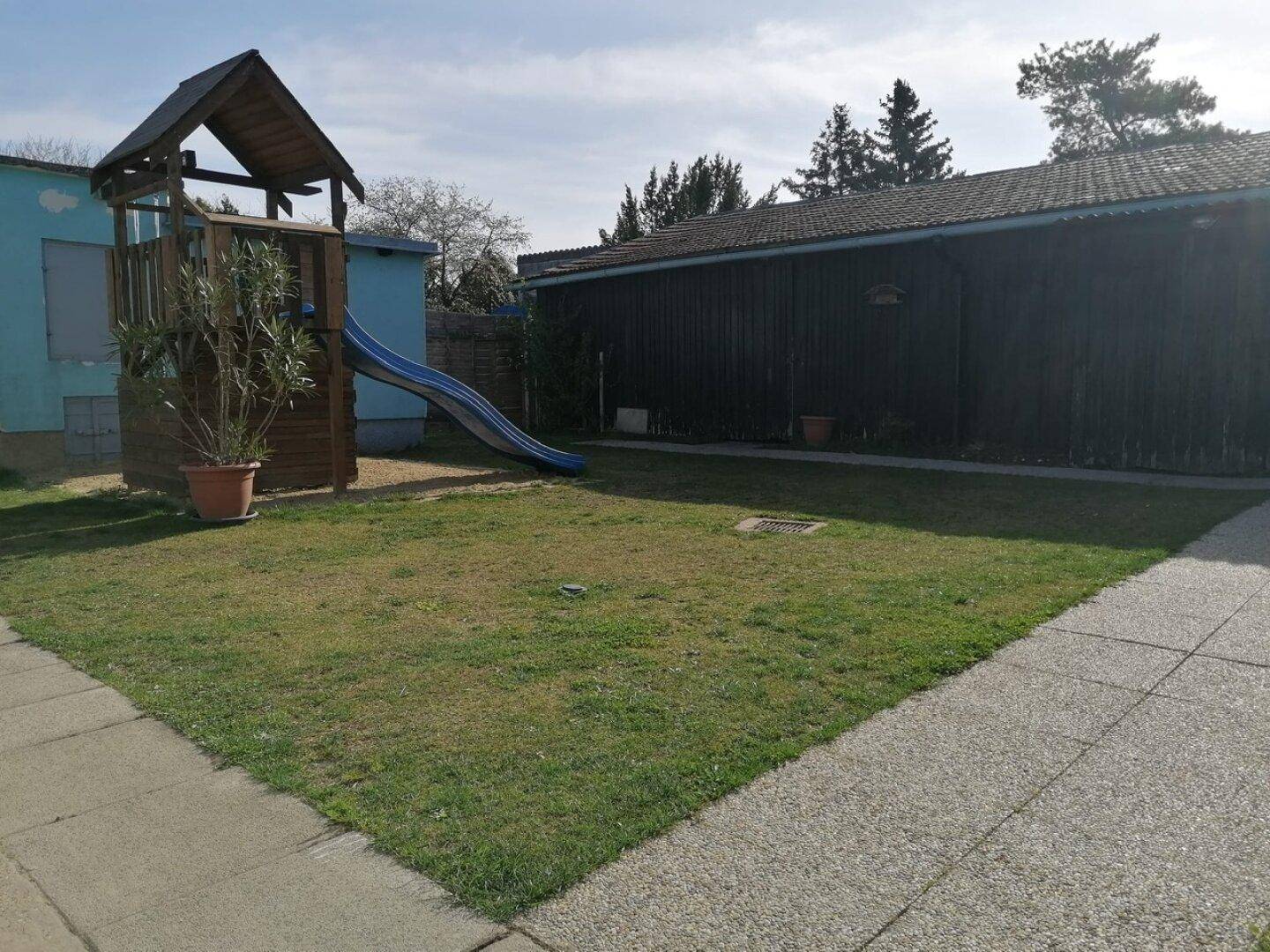 Gartenbereich mit Spielturm und Rutsche neben einem Nebengebäude.