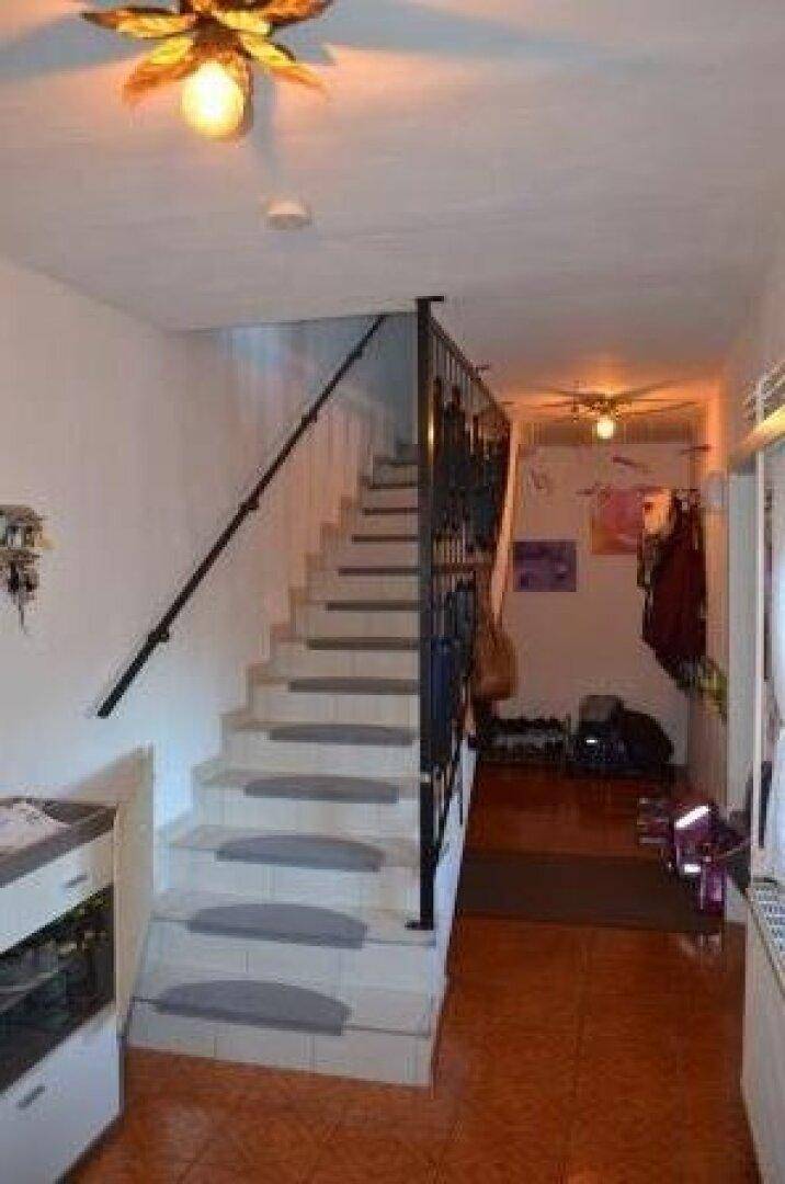 Heller Flur mit Treppe und Terrakotta-Fliesenboden, der zu den oberen Etagen führt.