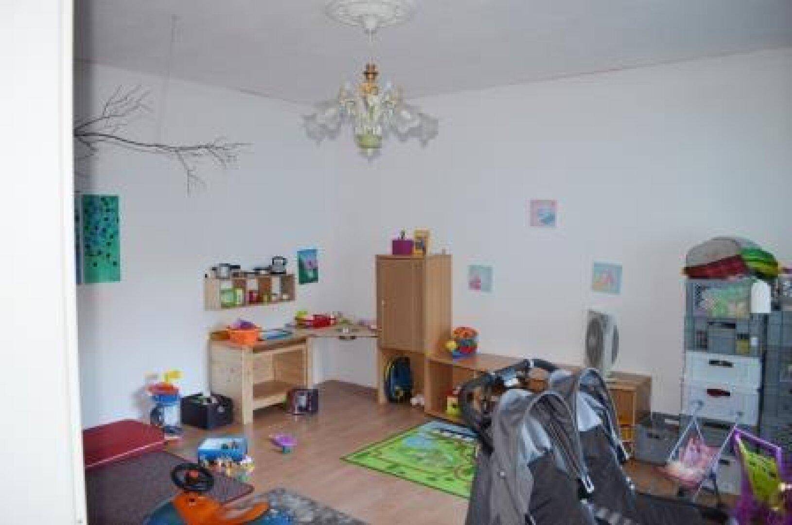 Heller Innenraum mit Spielzeug, Holzmöbeln und Laminatboden.